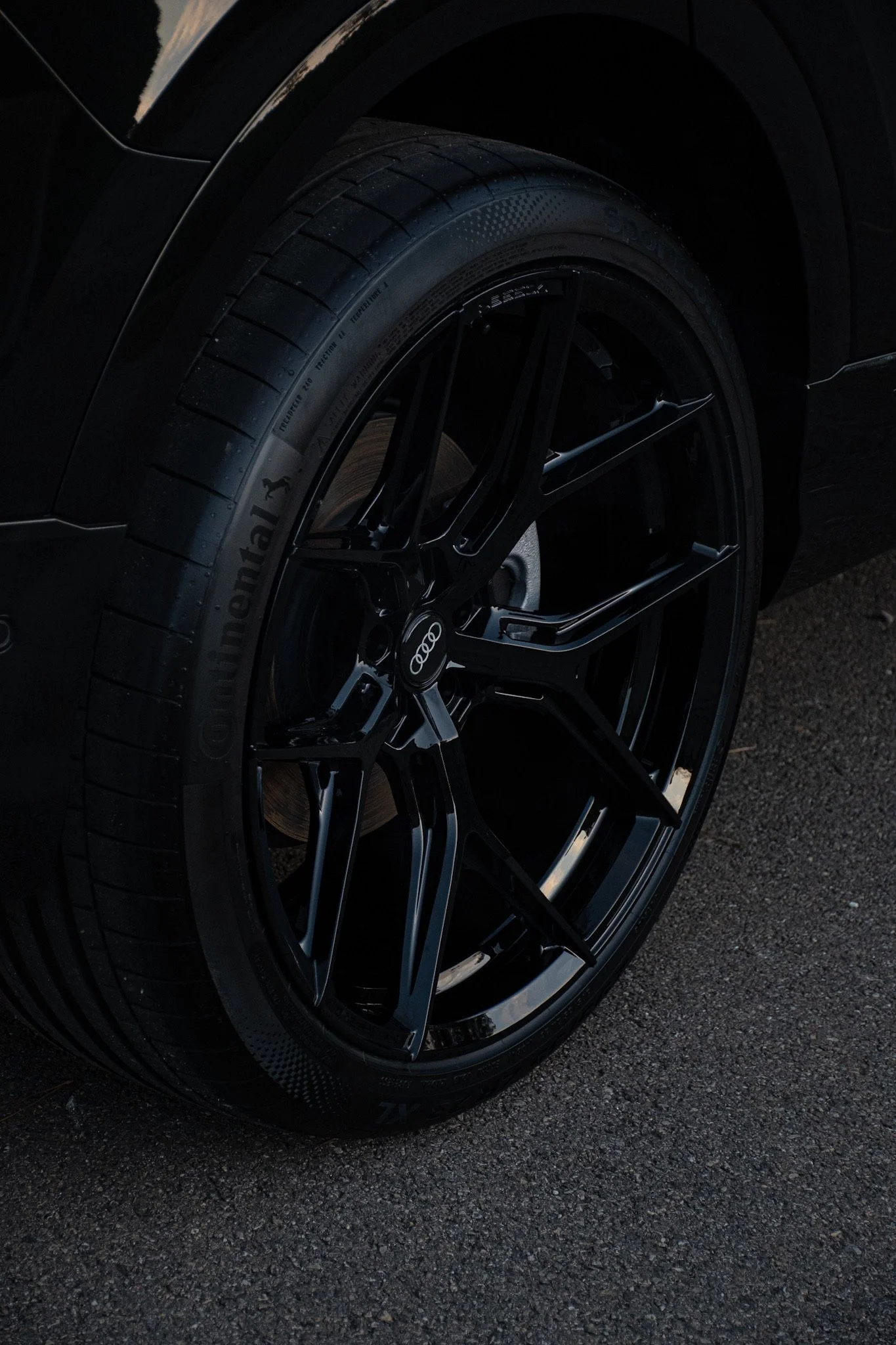 Close-up of a black tire and rim on a dark car, with a Volkswagen logo on the wheel hub, parked on an asphalt surface.