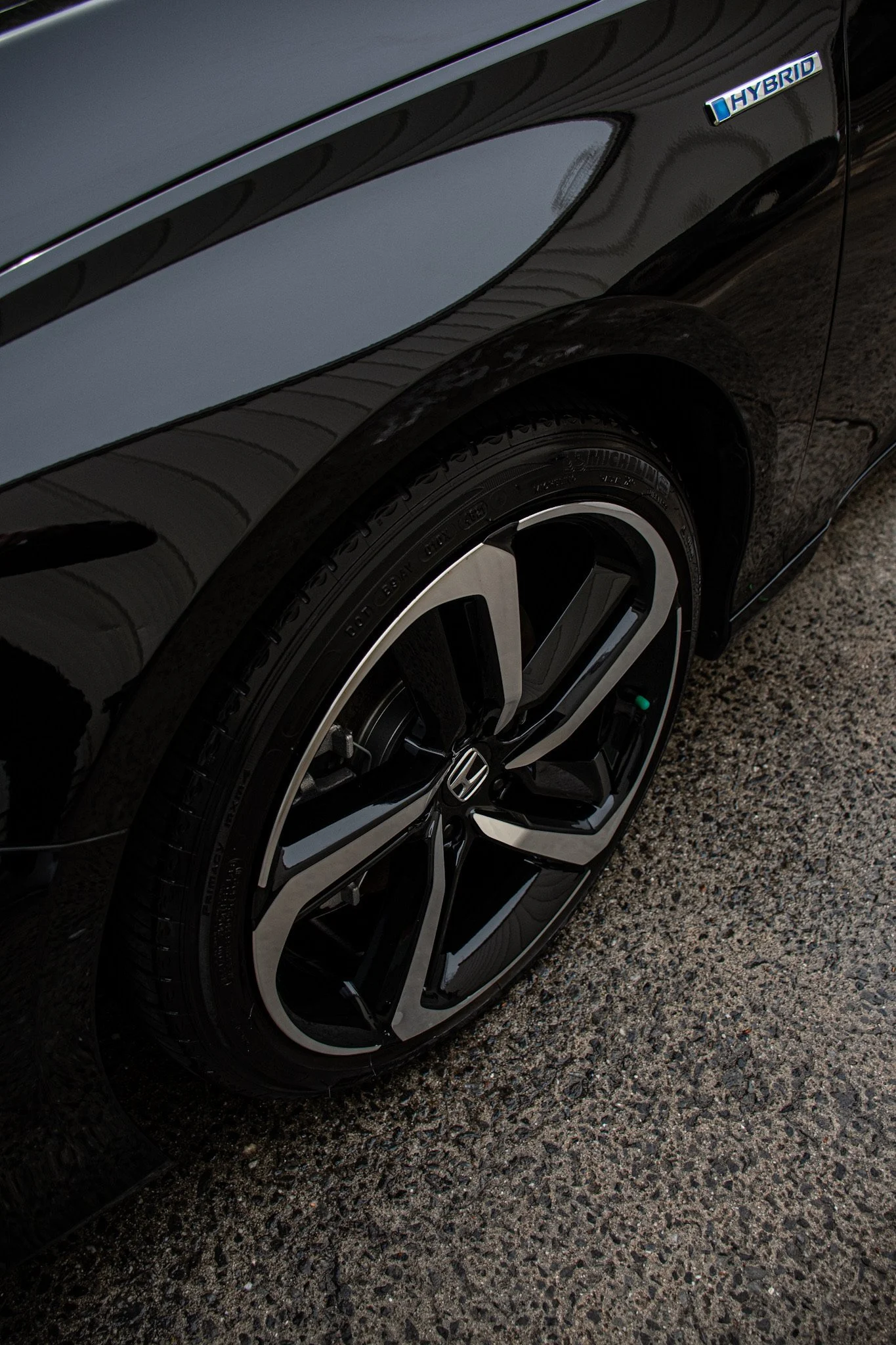 Close-up of a black car's front wheel and fender, with a hybrid badge on the side of the vehicle.