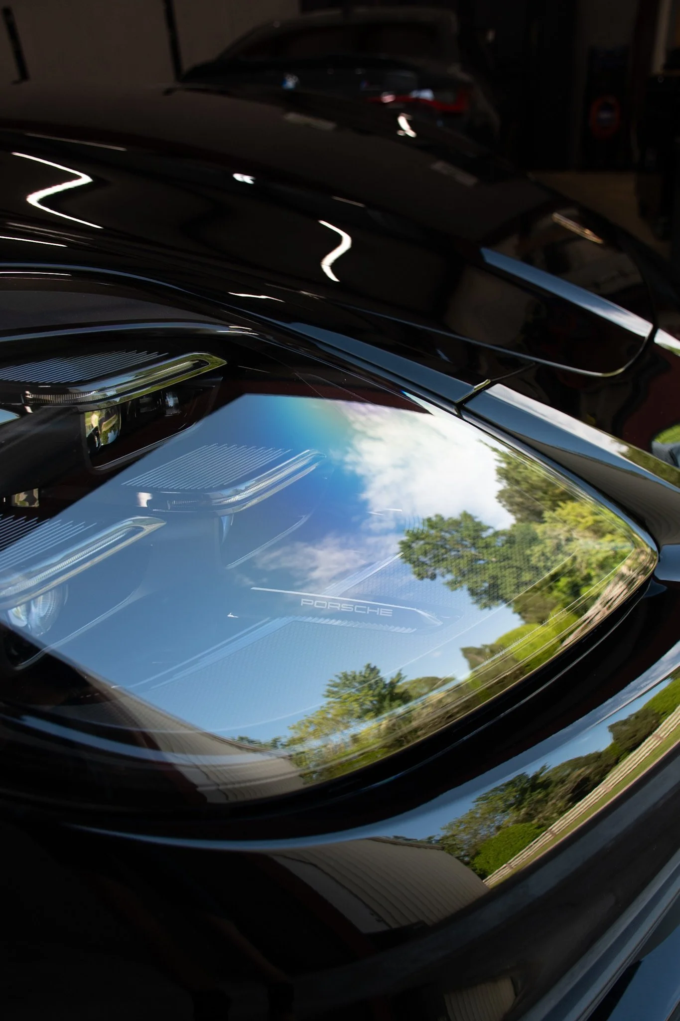 Close-up of a black Porsche car's front with a reflection of the sky and trees on the hood.