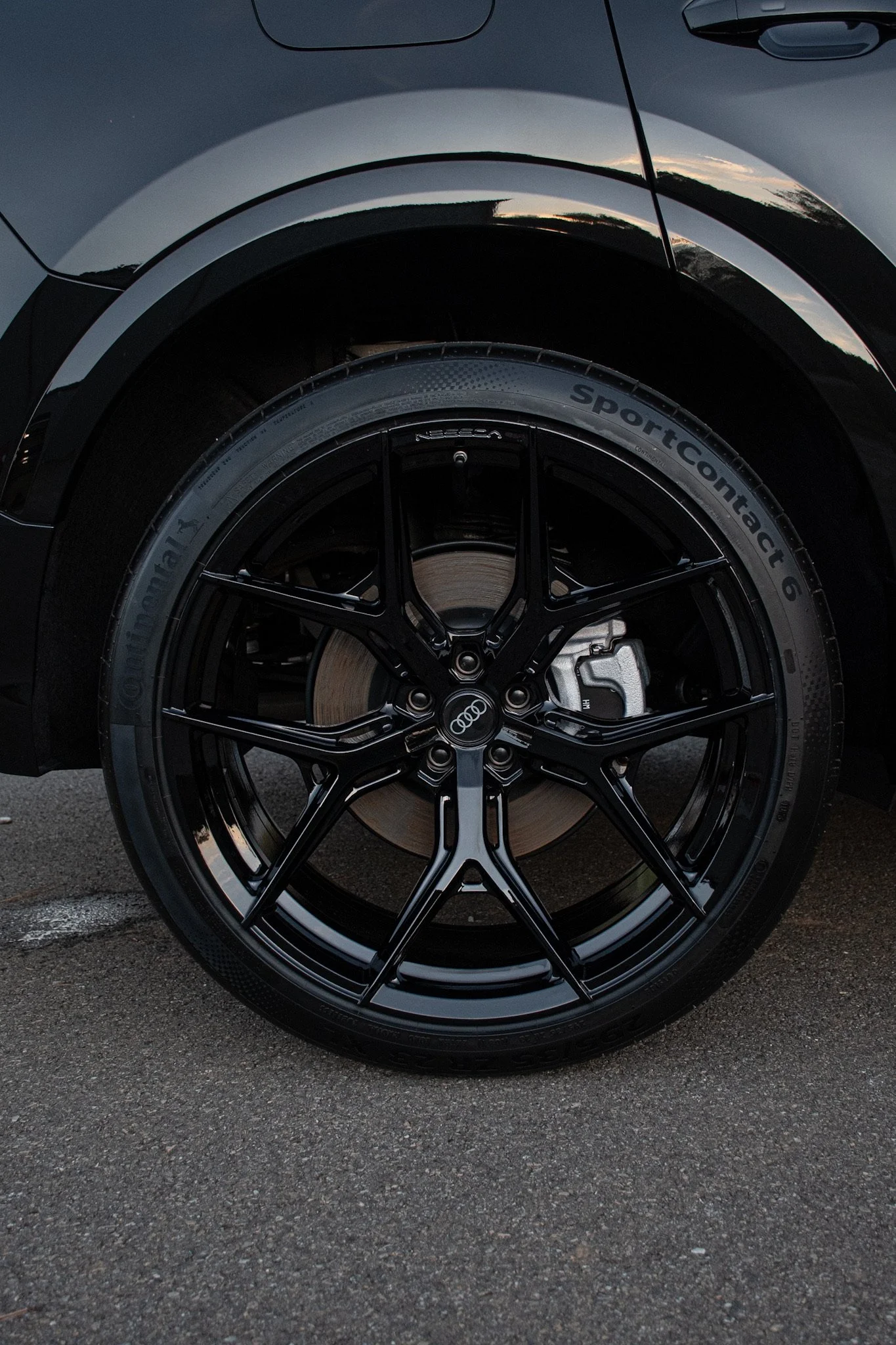 Close-up of a black Audi car wheel with a low-profile tire on an asphalt surface, reflecting the surroundings.