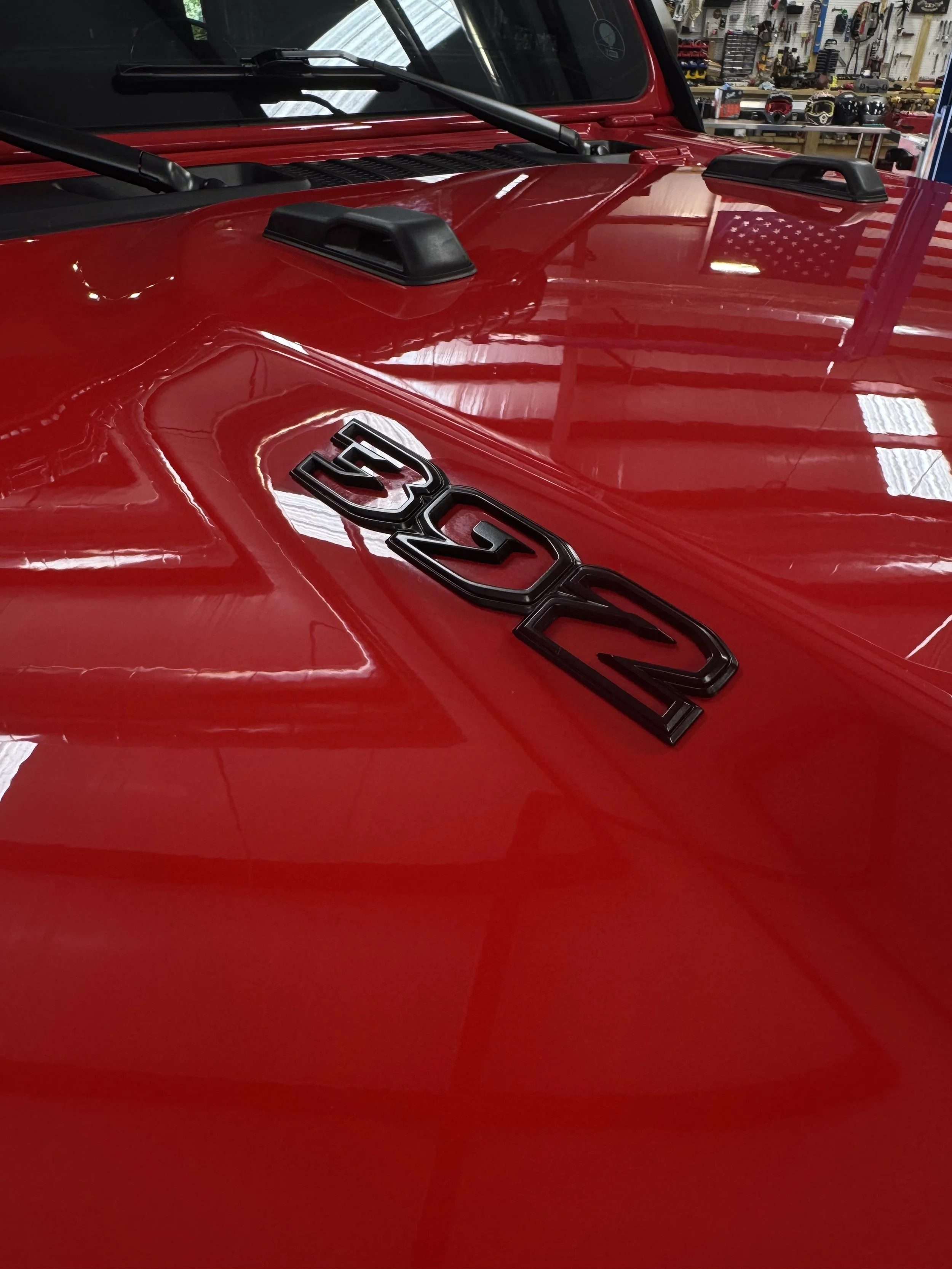 Close-up of a red Jeep with a 'Jeep' emblem on the hood, inside a garage or workshop with tools and equipment in the background.