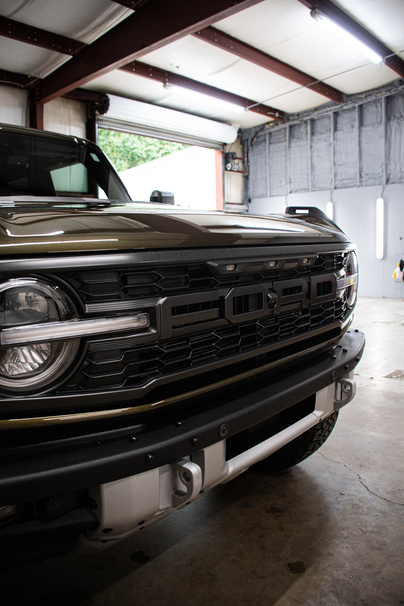 Close-up of a black Ford vehicle inside a garage, focusing on the front grille, headlight, and part of the bumper.