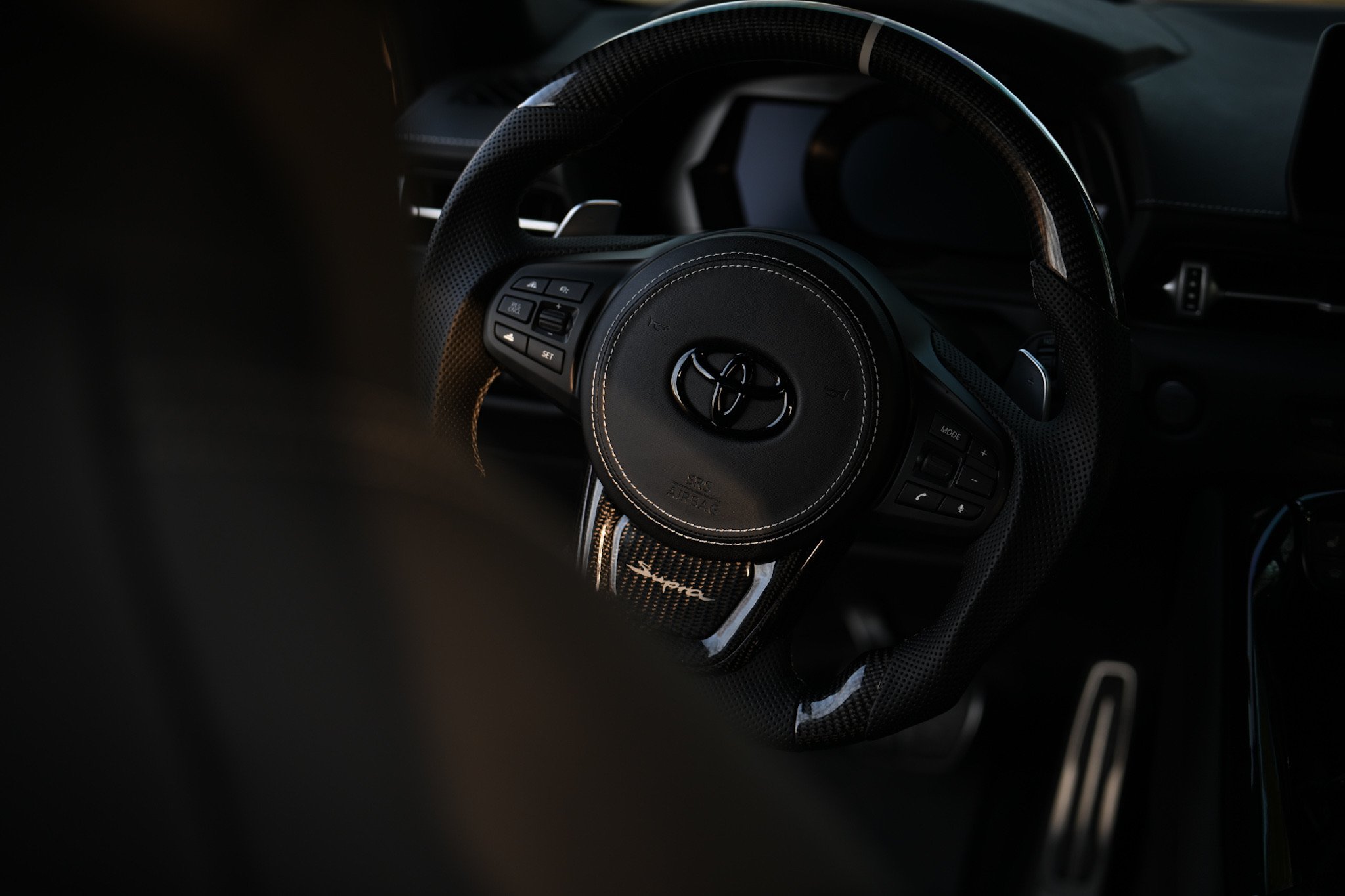 Close-up of a car steering wheel with a Toyota logo, featuring a black design with white stitching and controls on the sides.