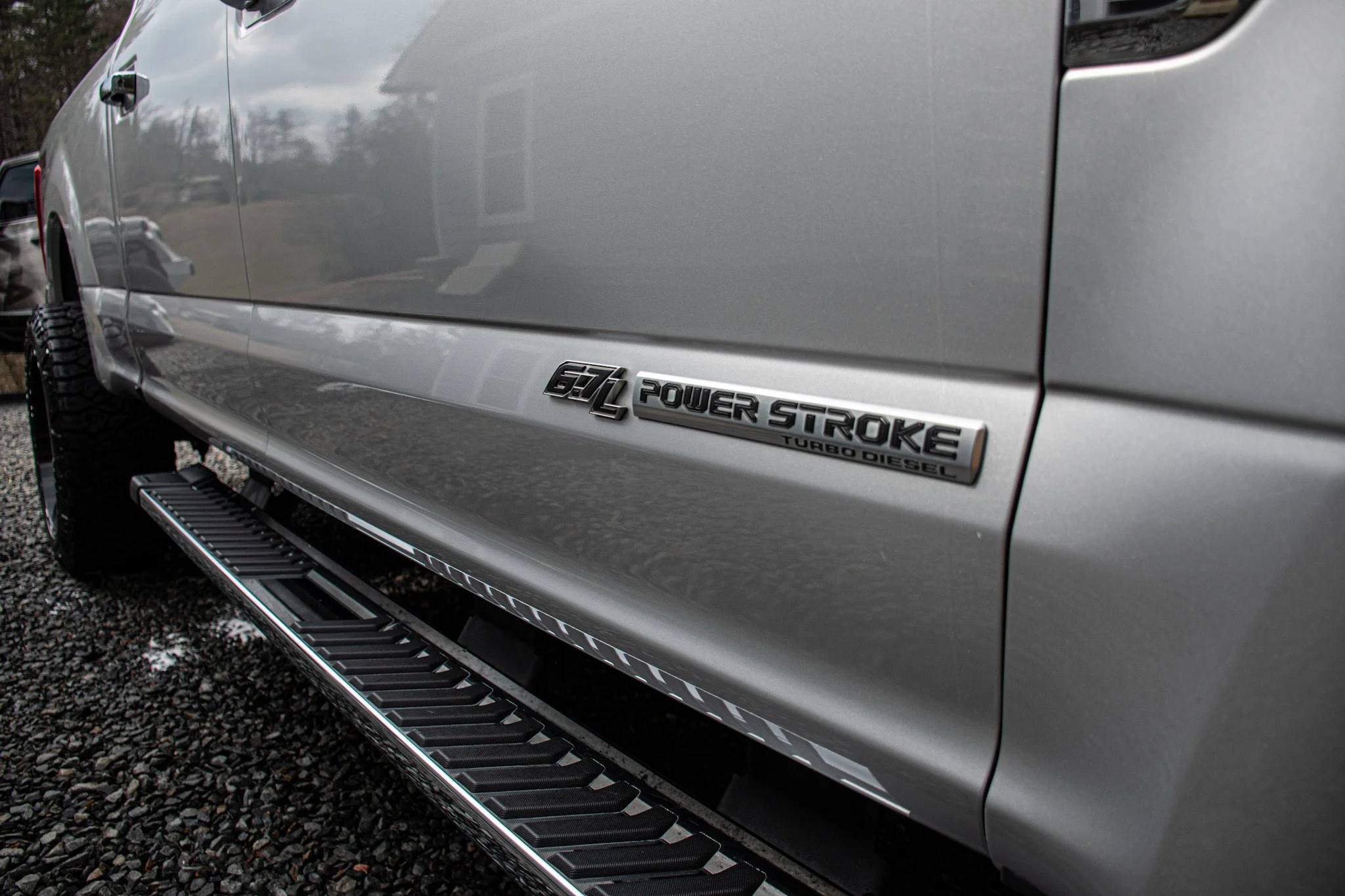 Close-up of the side of a silver pickup truck with a badge reading 'GTL Power Stroke Turbo Diesel' and black and silver side steps.