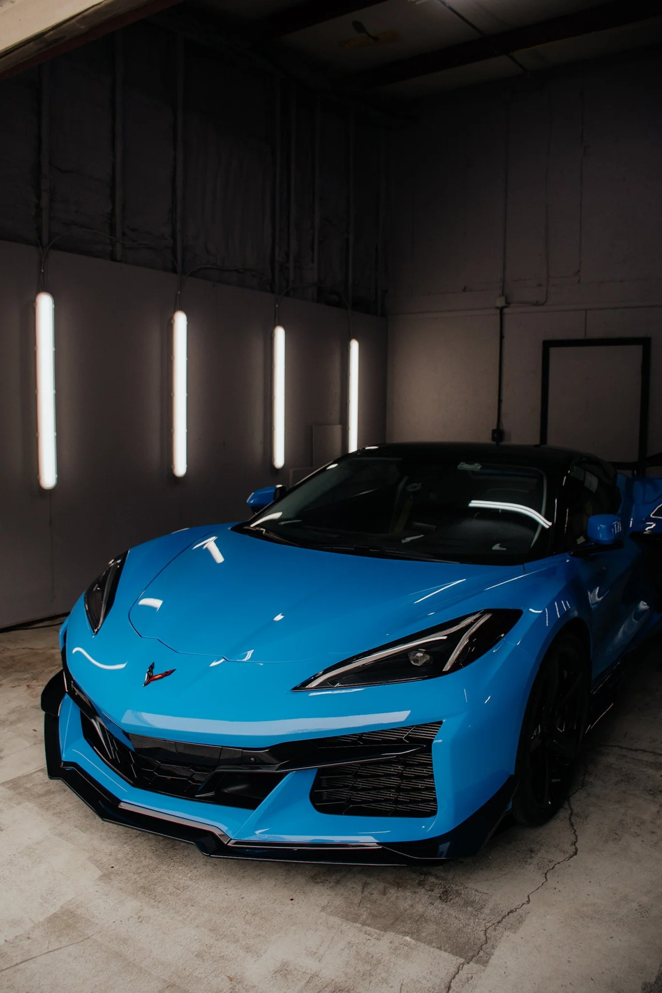 Blue sports car in a showroom or garage with dark wall and vertical white neon lights.