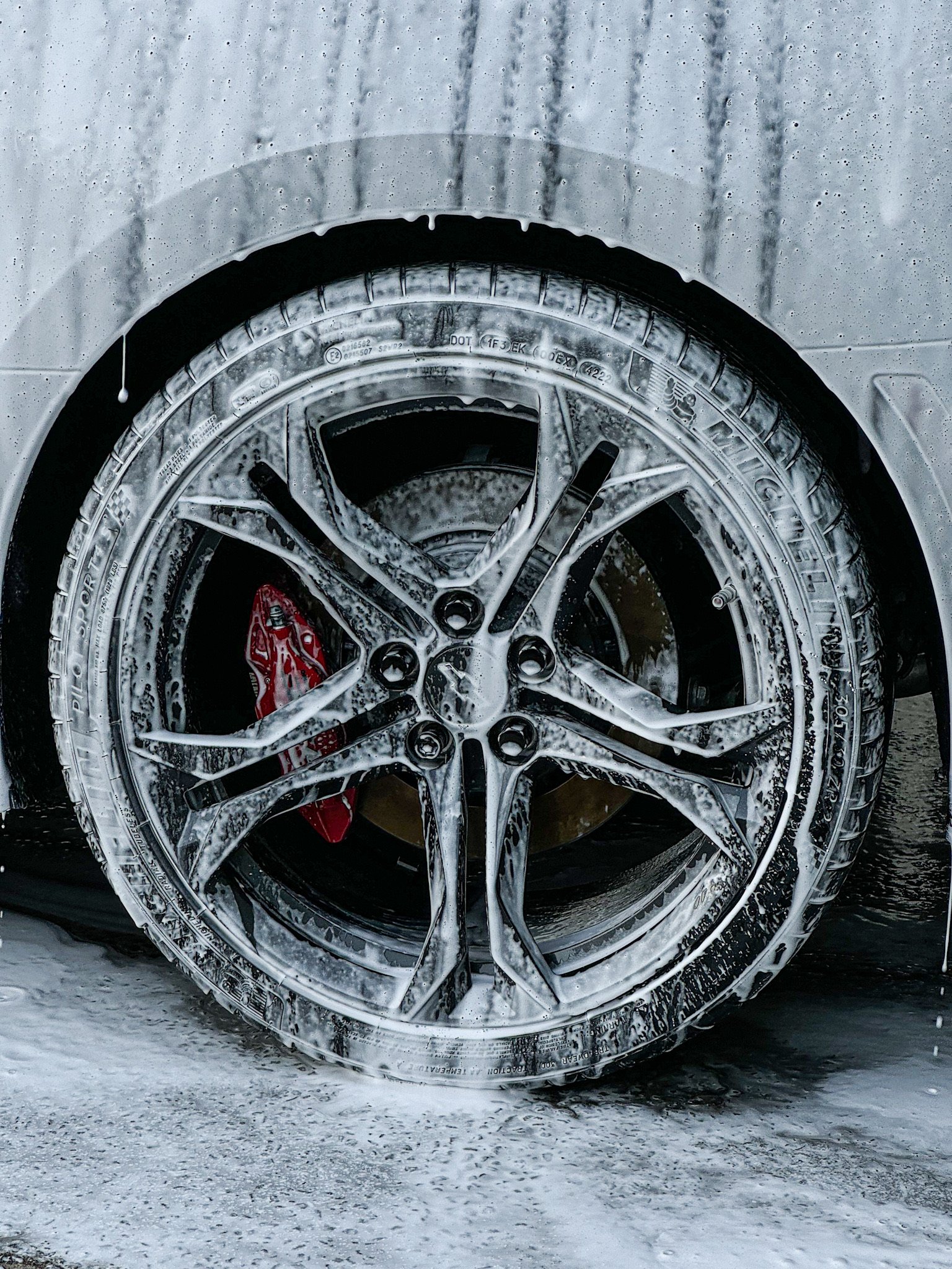 Close-up of a car wheel being washed with soap and water, suds covering the rim and tire.