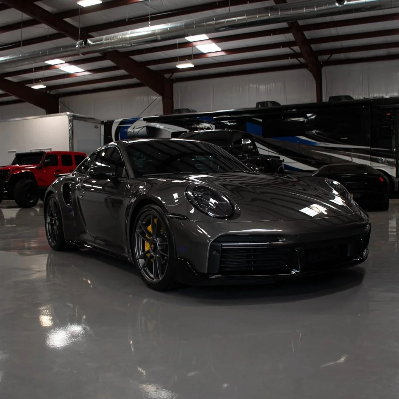 A dark gray Porsche sports car parked inside a spacious warehouse or garage with a high ceiling, metal beams, and industrial lighting.