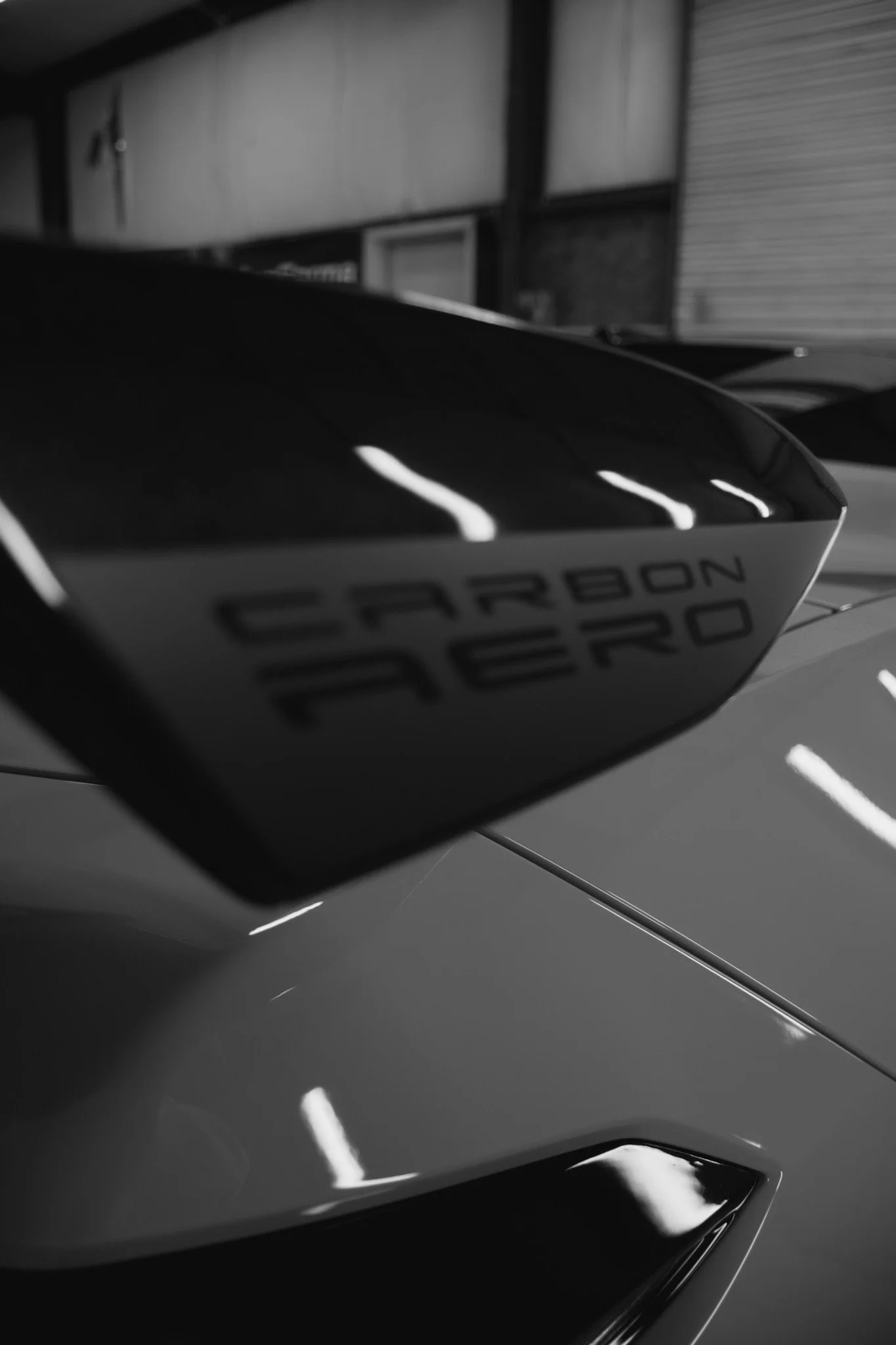 Close-up black-and-white photo of a sleek car with a focus on the rear wing, displaying the words 'CARBON CERVO' on the side.