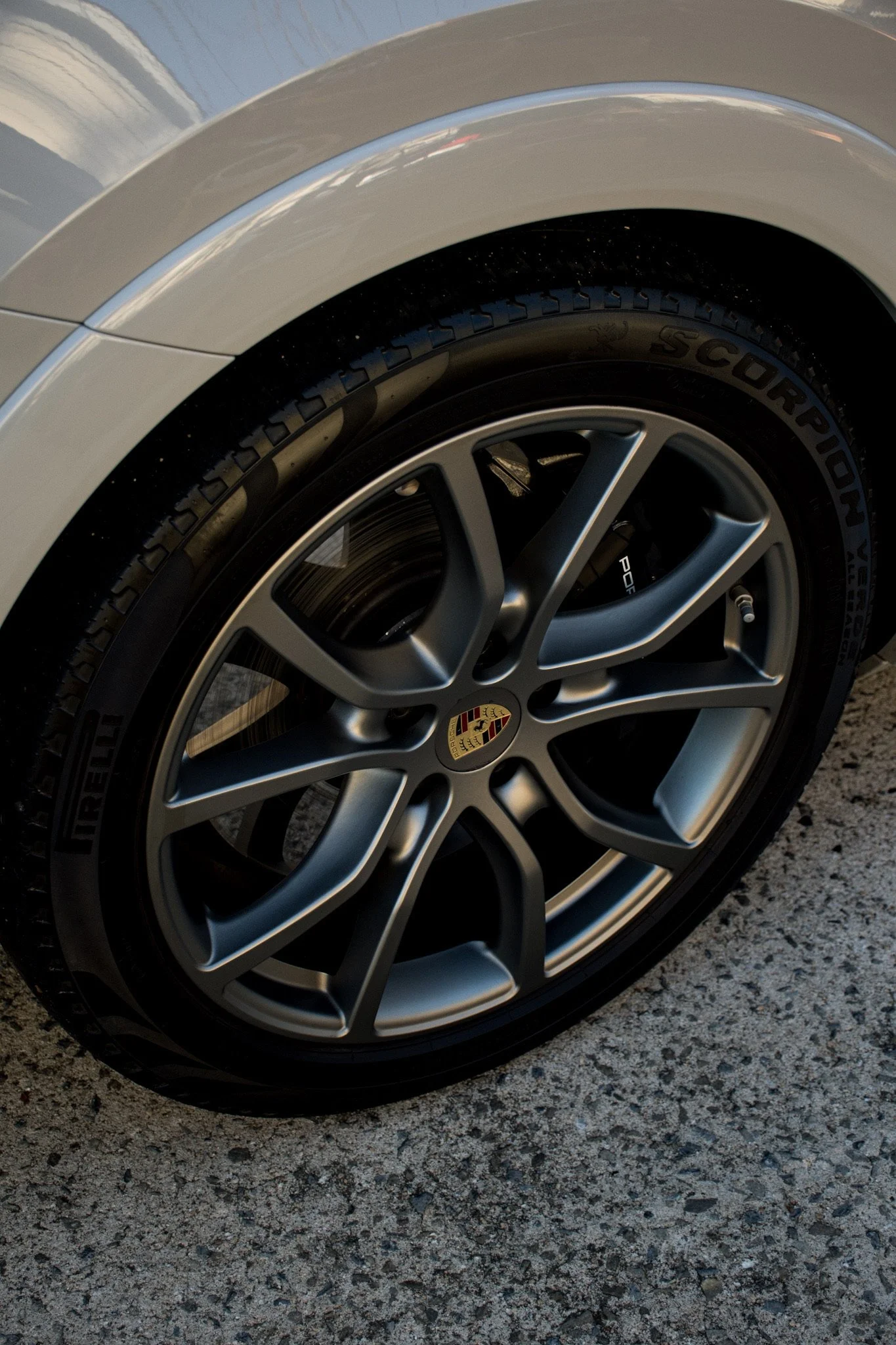 Close-up of a silver Porsche car wheel with a black tire on a rough asphalt surface.