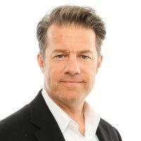 Portrait of a middle-aged man with gray hair wearing a black suit and white shirt, looking at the camera.