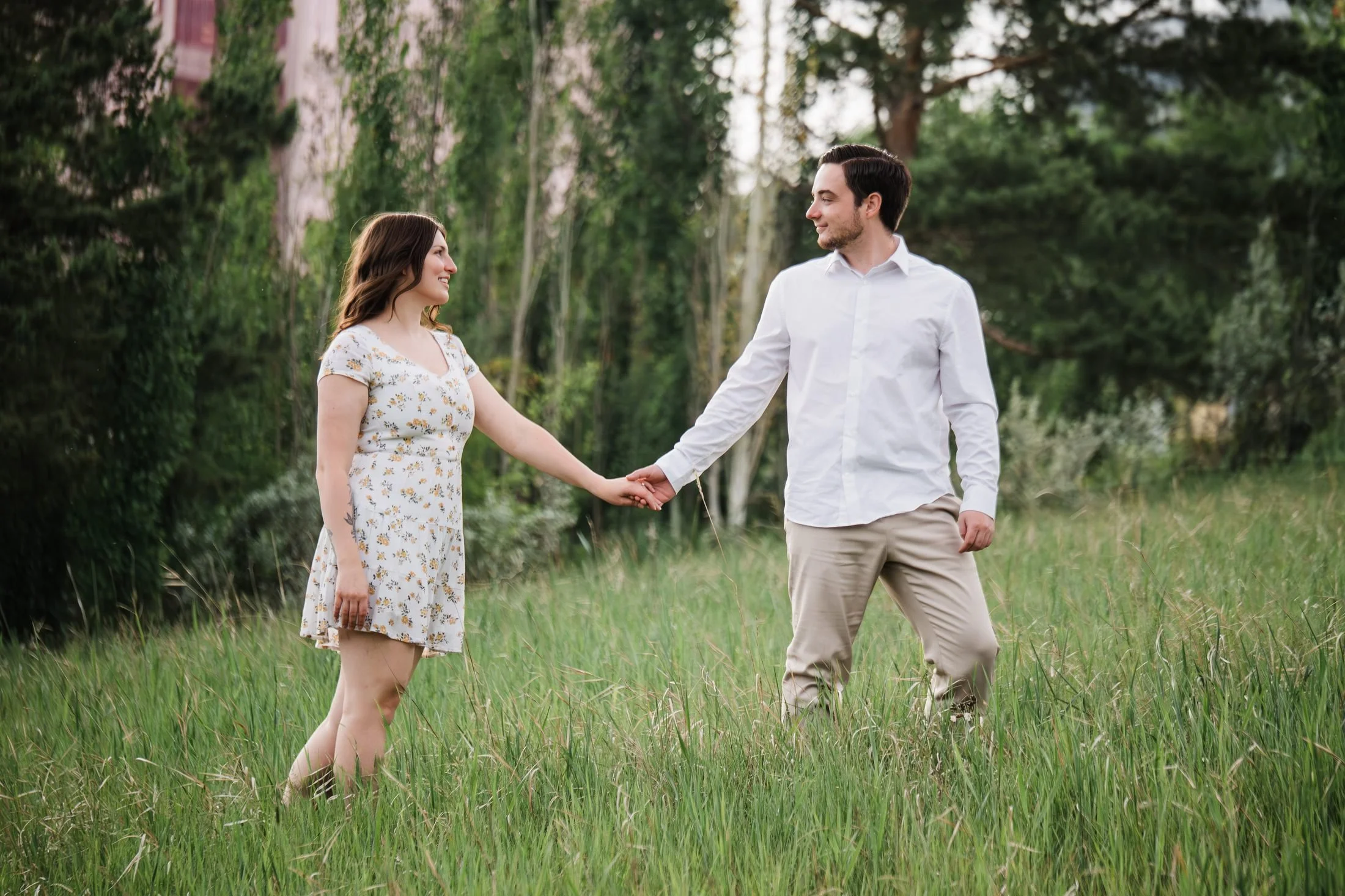 Couple holding hands and smiling at each other during an outdoor engagement session in Edmonton’s river valley.