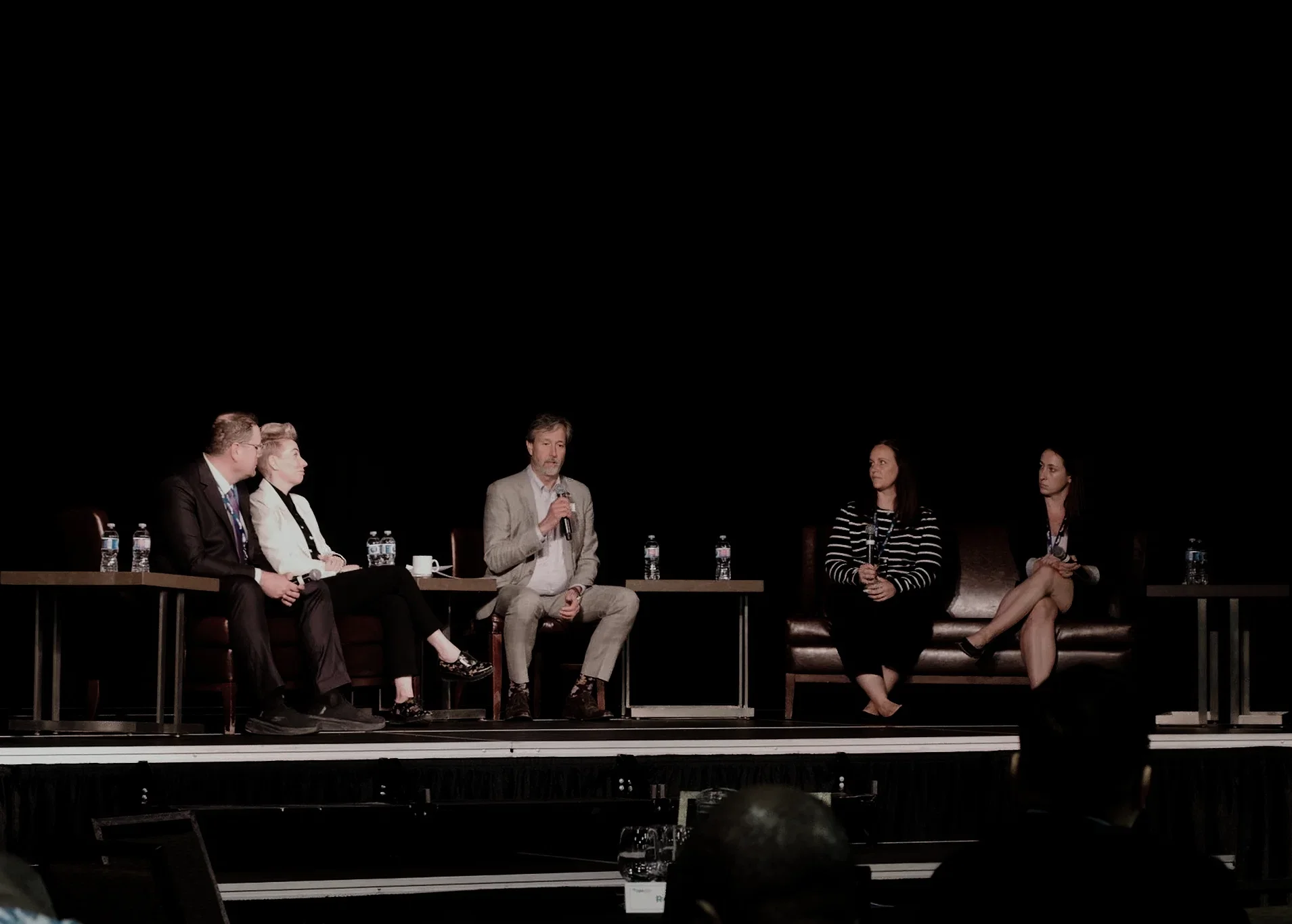 Five speakers take part in a panel discussion on stage during a live event.
