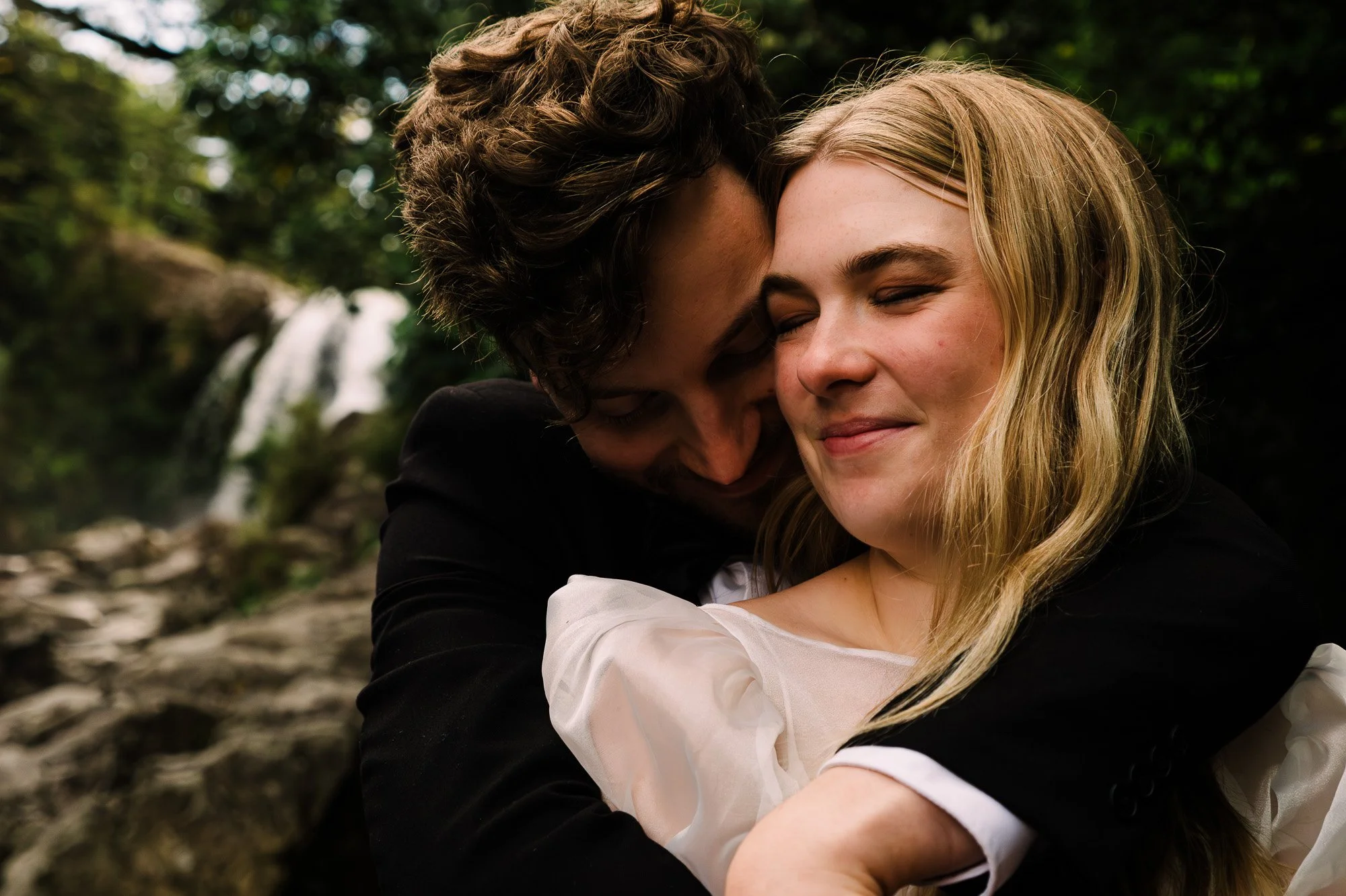 Styled elopement couple holding each other with Tawhai Falls in the background during a New Zealand elopement photography session by Kevin M Films.