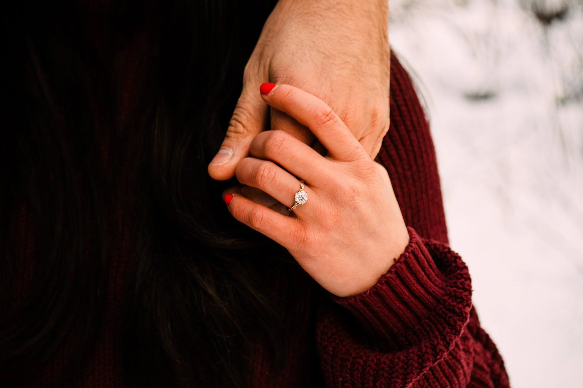 Close-up of an engagement ring while a couple holds hands in the snow at Whitemud Ravine during an Edmonton engagement photography session by Kevin M Films.