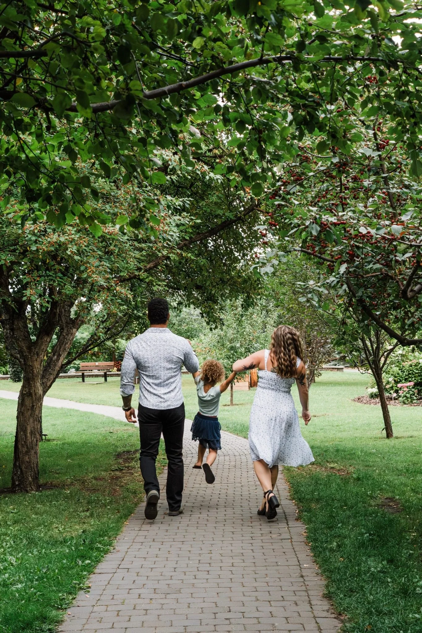Family walking hand in hand through St. Albert Botanic Park during an Edmonton family photography session by Kevin M Films.