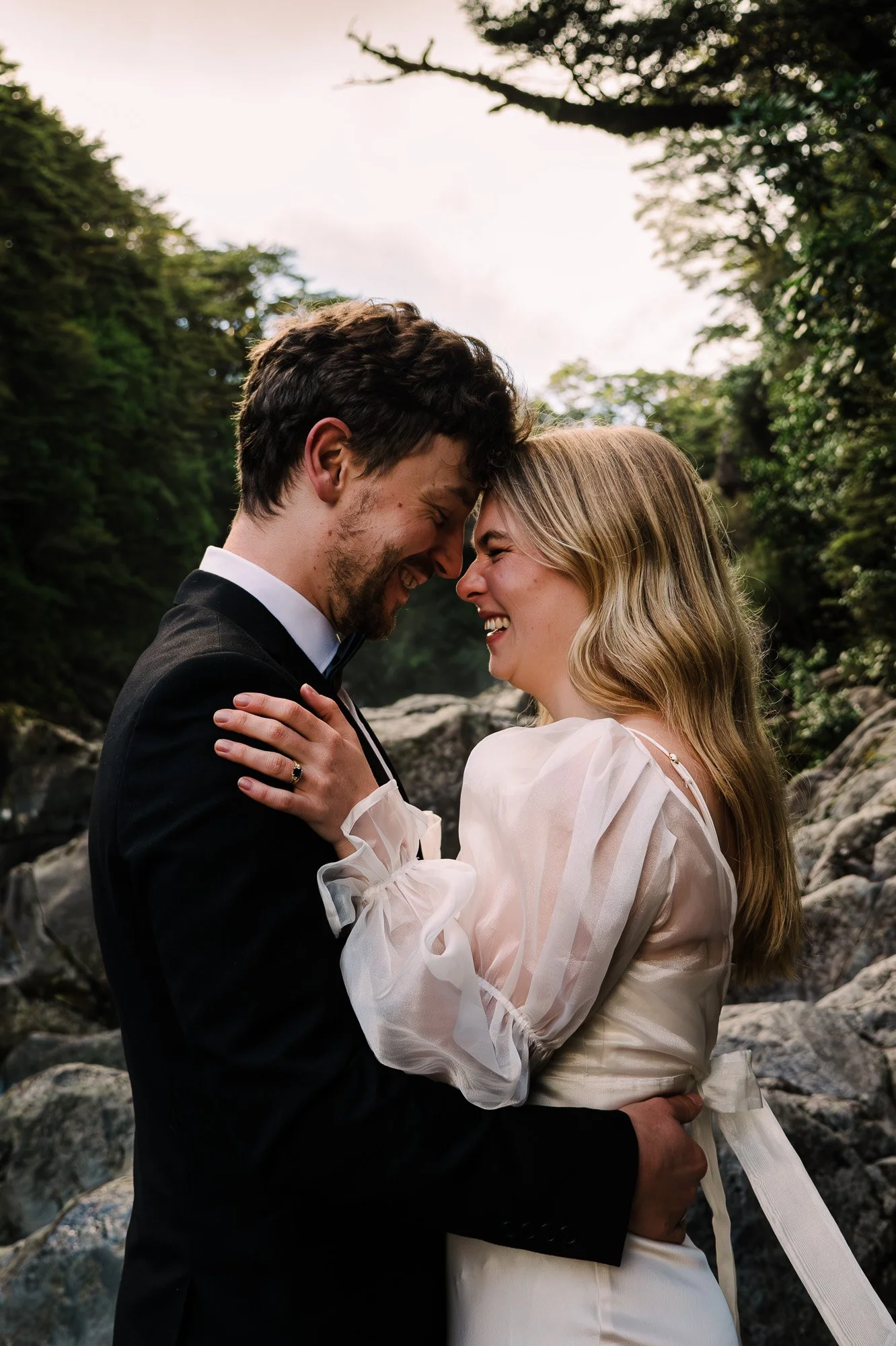 Styled elopement couple sharing a joyful portrait near Tawhai Falls during a New Zealand elopement photography session by Kevin M Films.