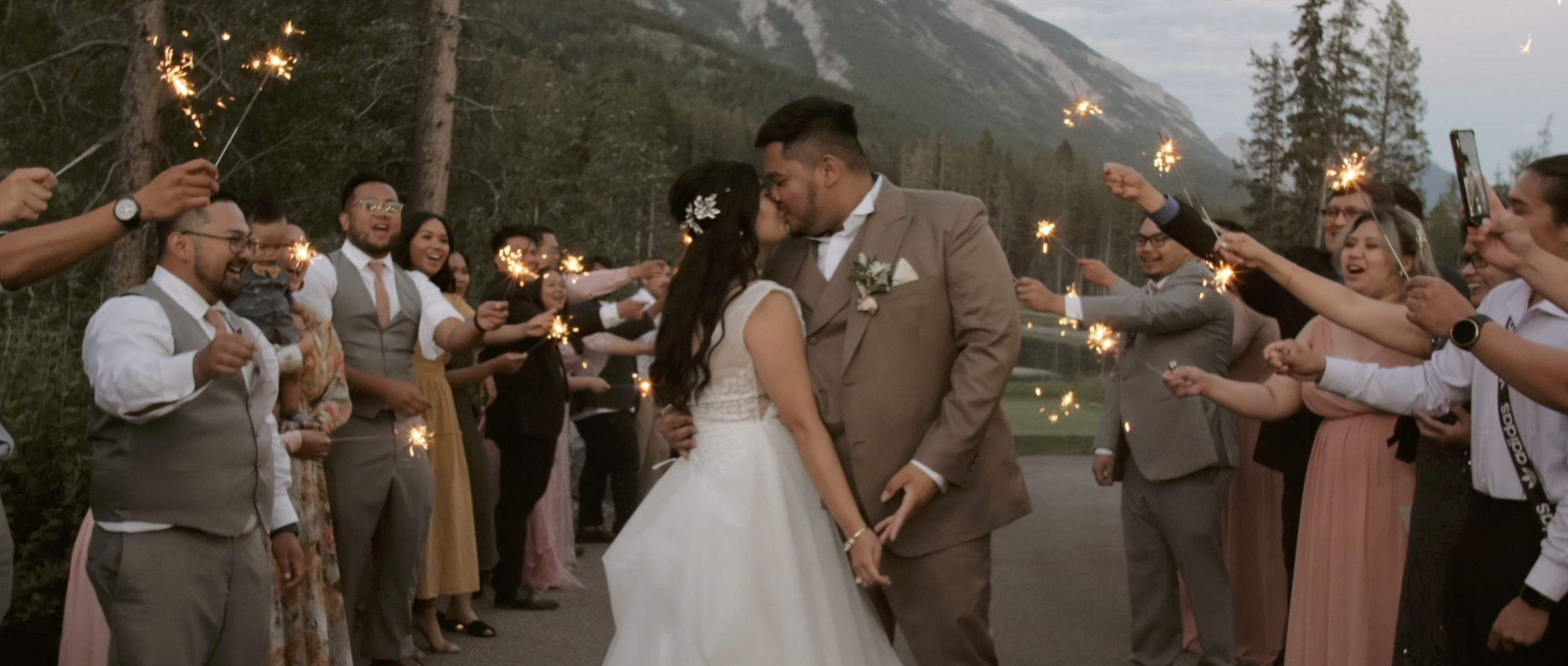 Bride and groom kissing in the rocky mountains, surrounded by their guests with sparklers
