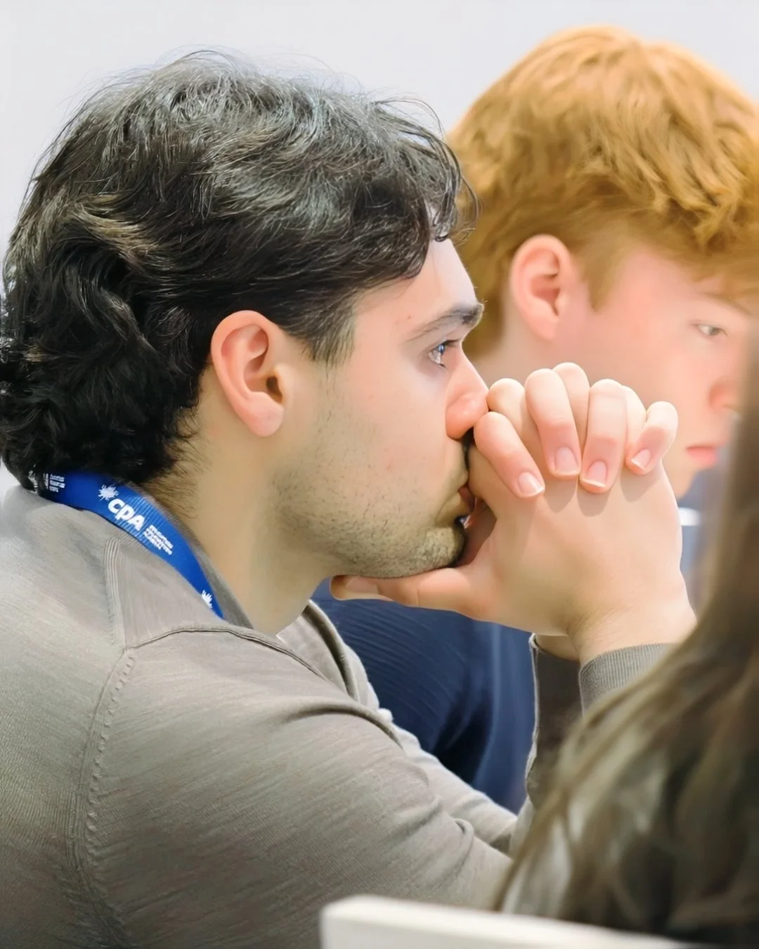 Event attendee listening with clasped hands near his face, seated beside another participant.