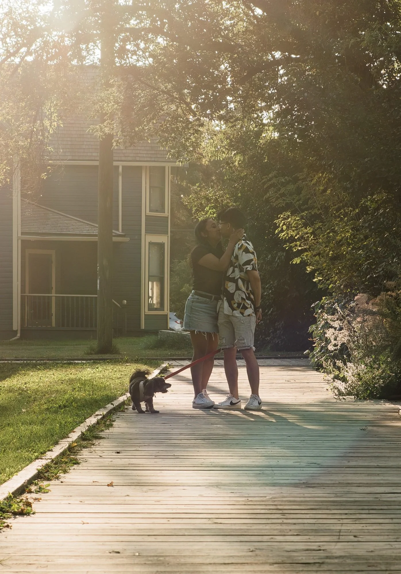 Couple kissing on a sunlit boardwalk with their dog during an Edmonton couples photography session by Kevin M Films.