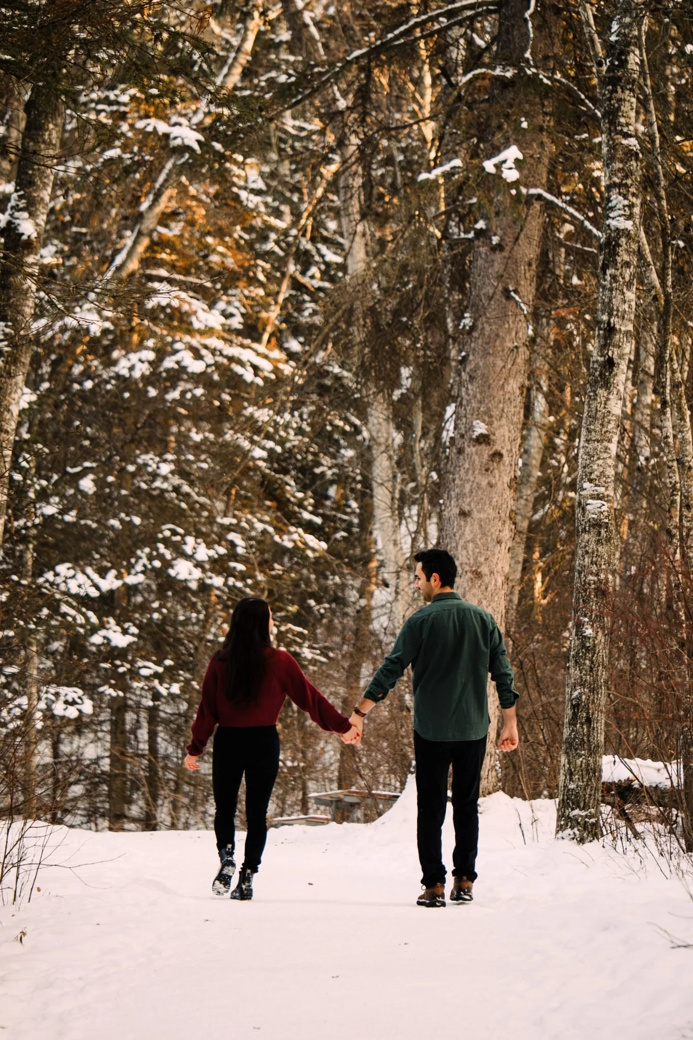 Engaged couple walking hand in hand through snowy trees at Whitemud Ravine during an Edmonton engagement photography session by Kevin M Films.