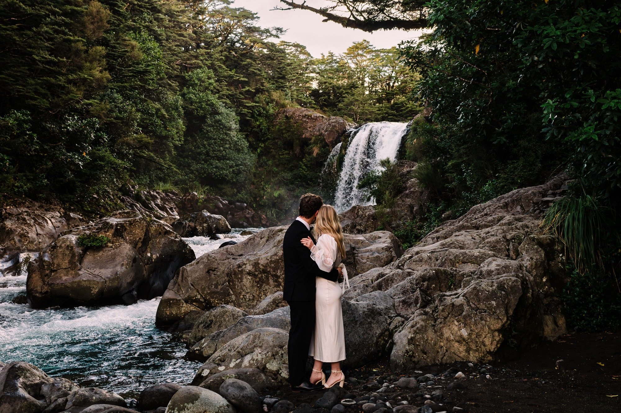 Styled elopement couple standing beside Tawhai Falls, also known as Gollum’s Pool, in New Zealand, photographed by Kevin M Films.