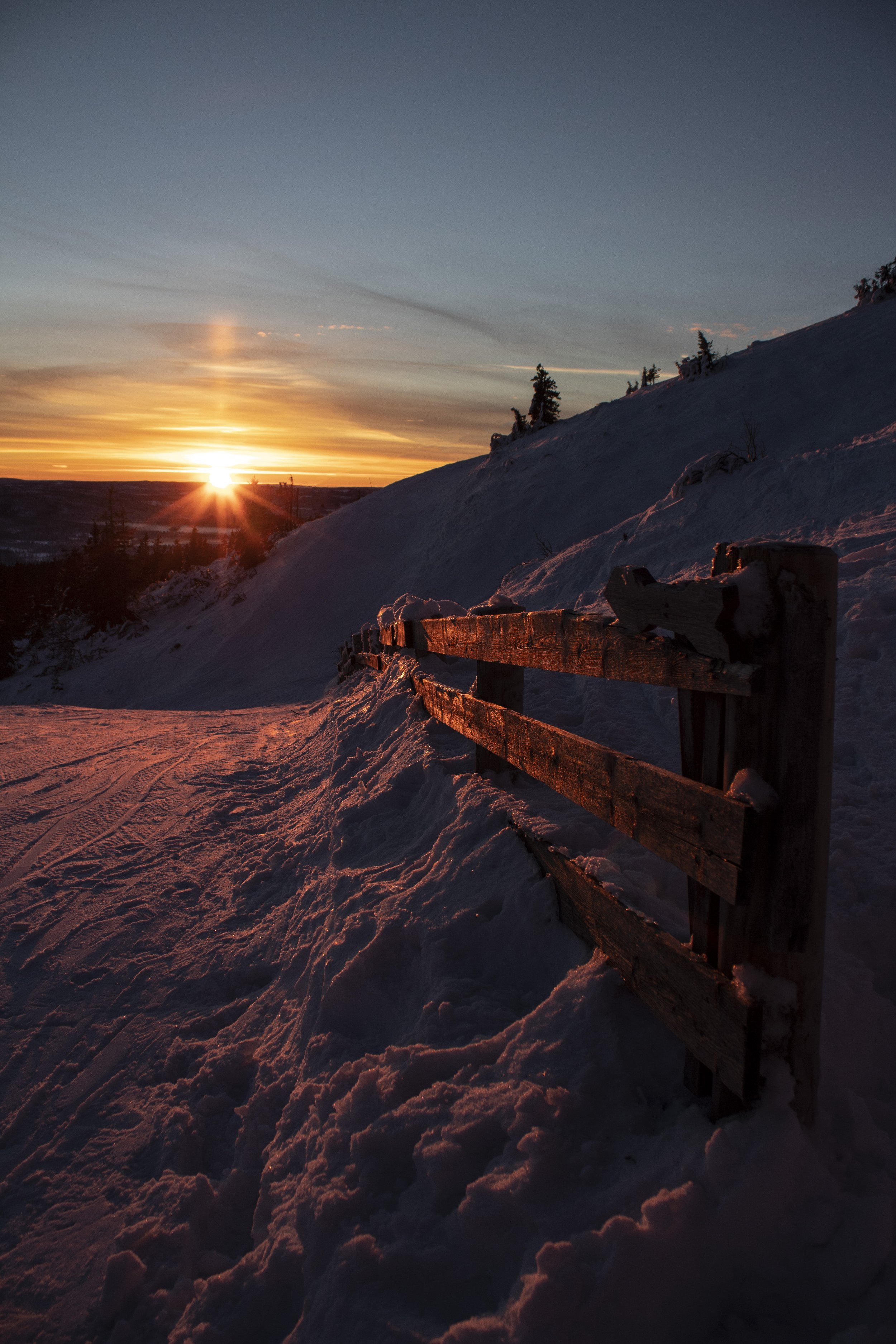 Sunset winter landscape with snow-covered slope and wooden fence