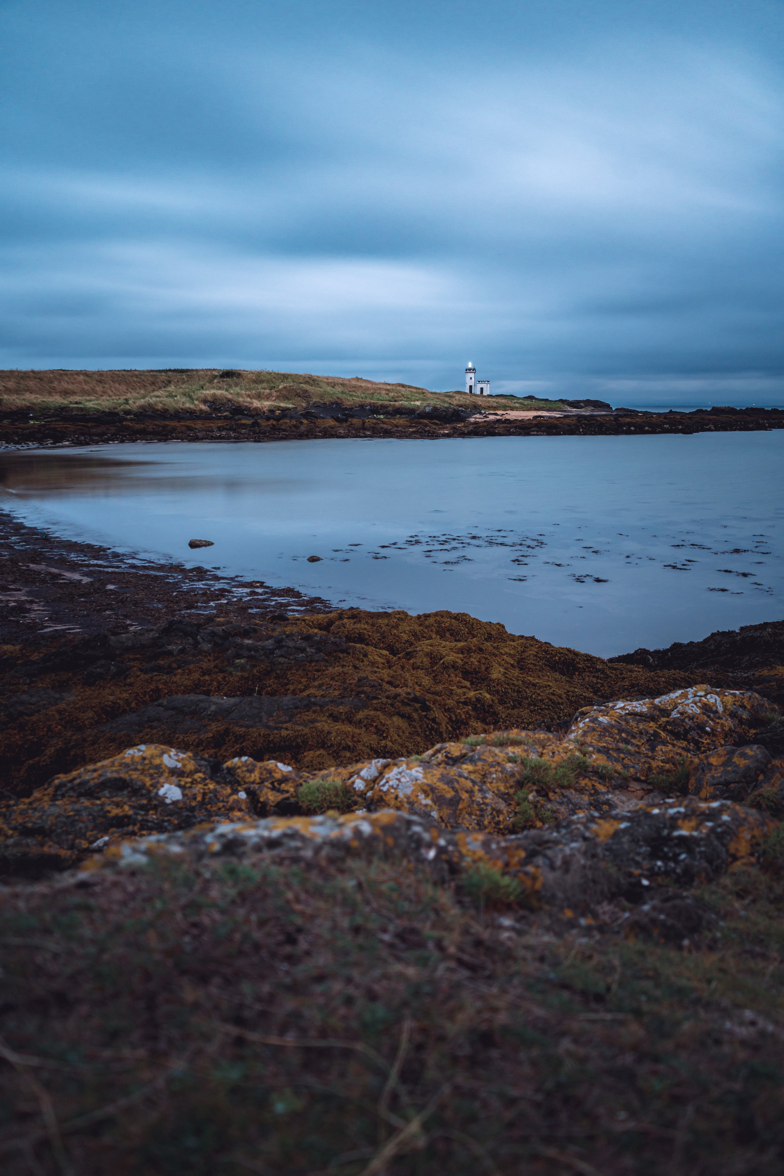 Coastal landscape with lighthouse under cloudy sky.