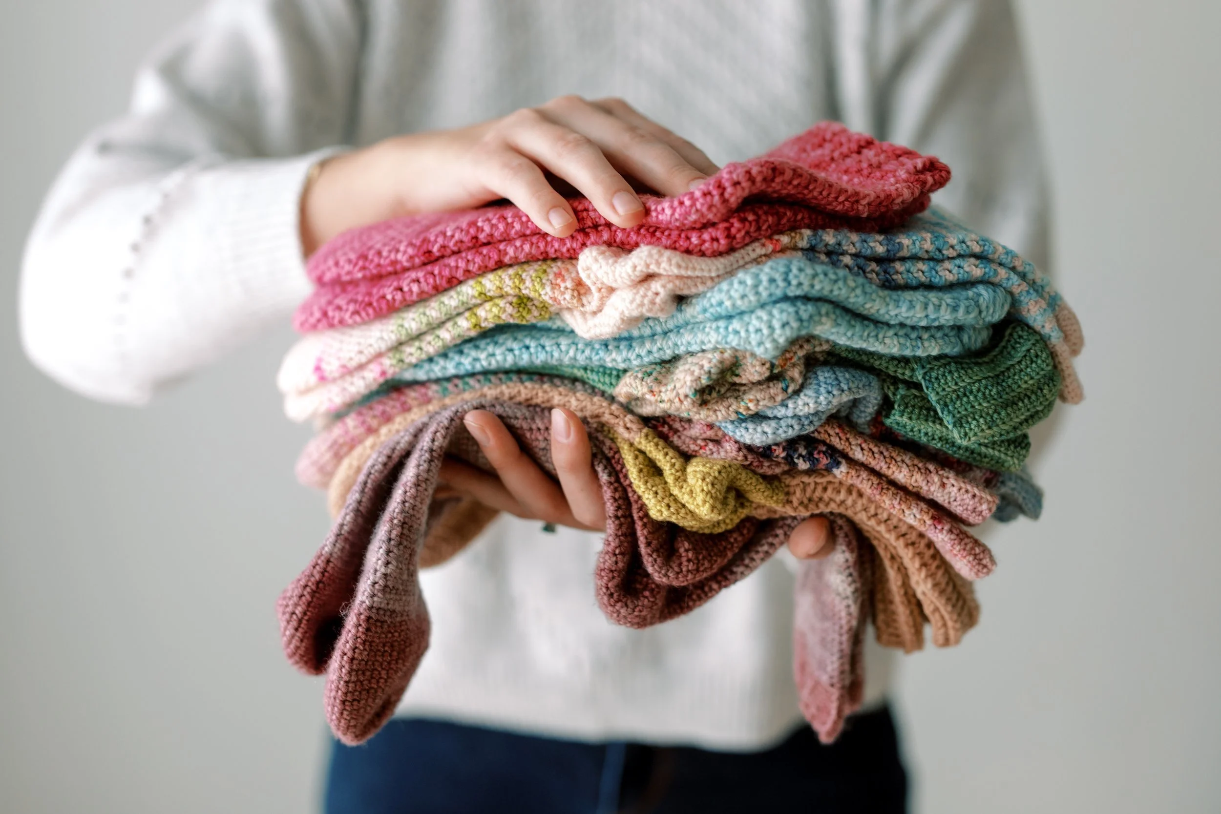 A person holding a large pile of multicolored crocheted socks.