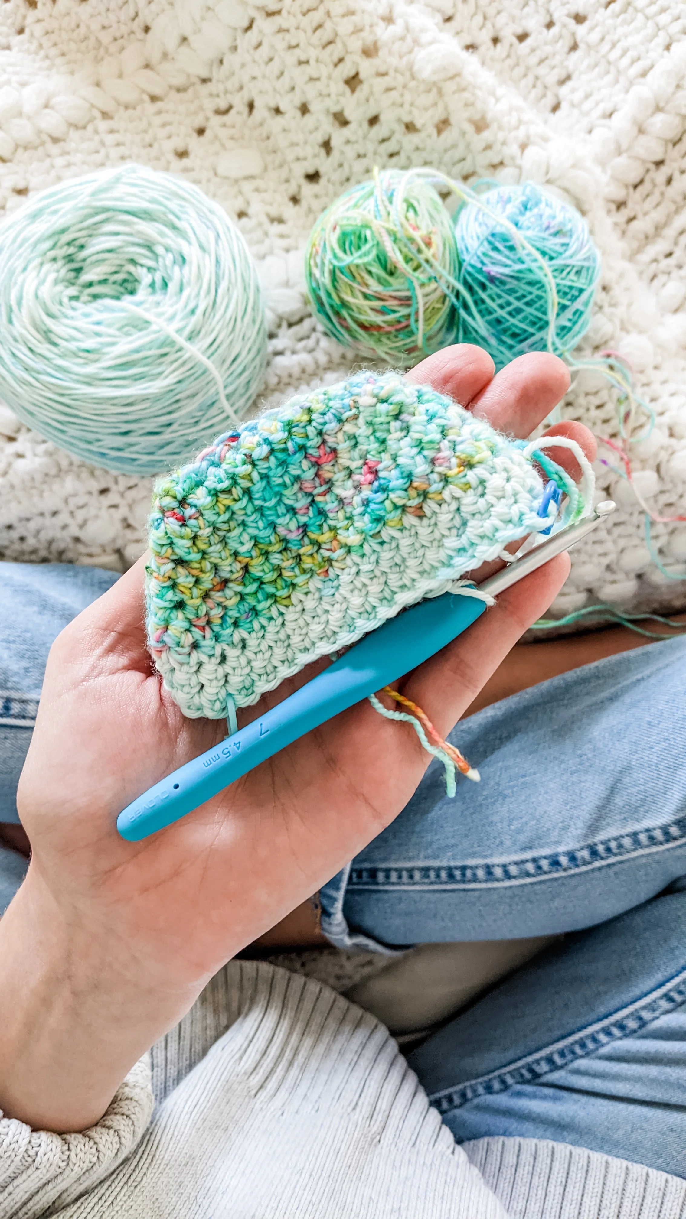 A person crocheting with multicolored yarn, sitting on a knitted blanket with yarn balls nearby.