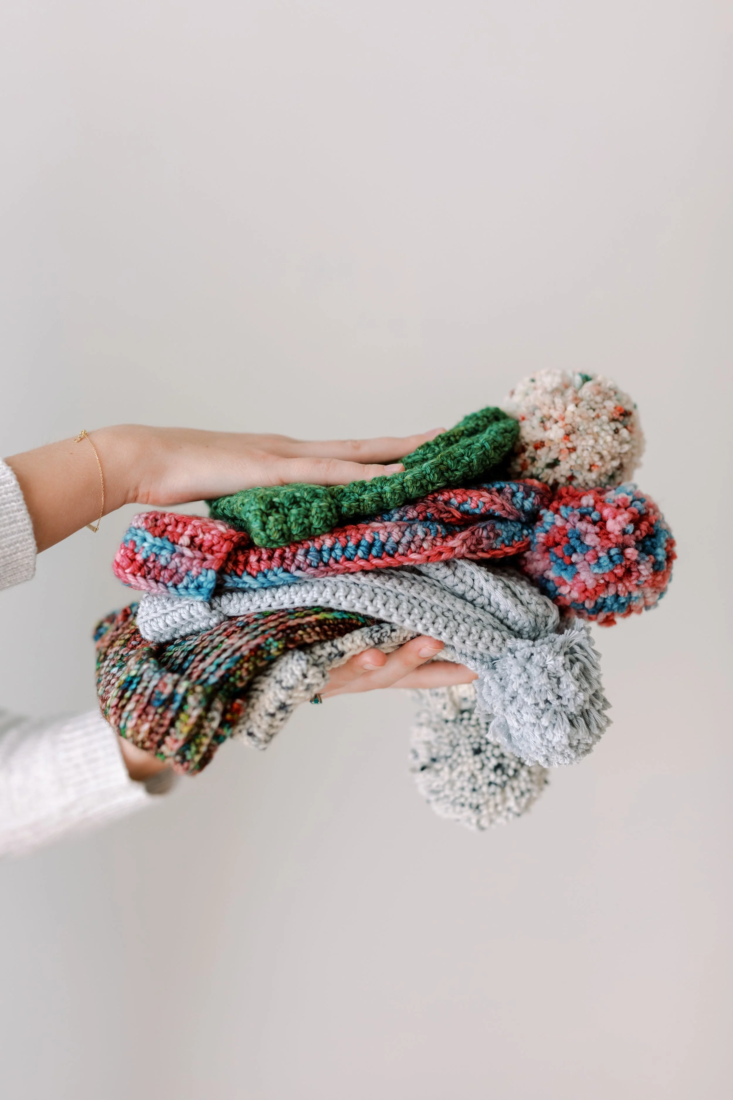 Person holding a pile of colorful knitted hats, with a plain white background.