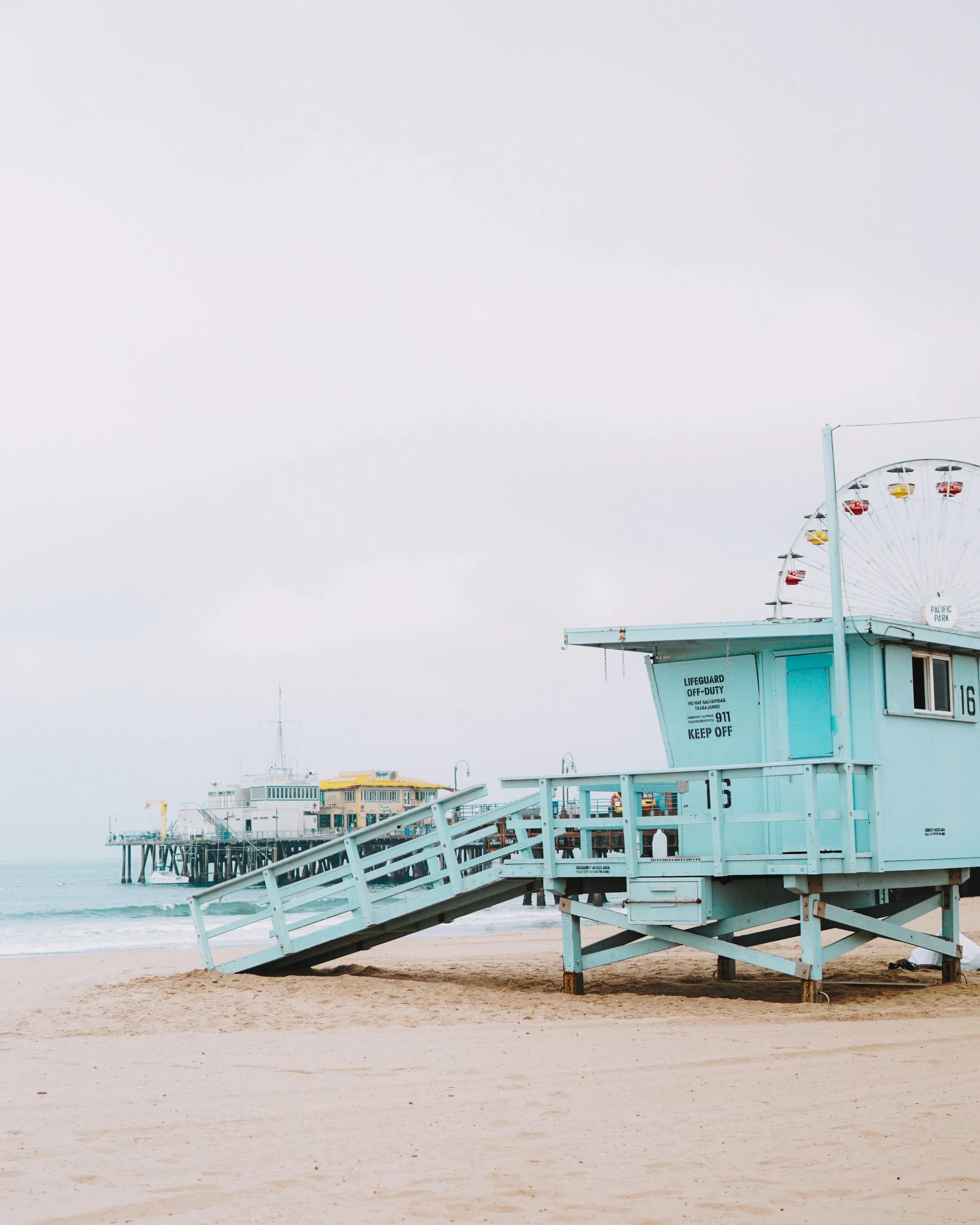 A lifeguard station on a sandy beach with a Ferris wheel in the background and overcast sky.