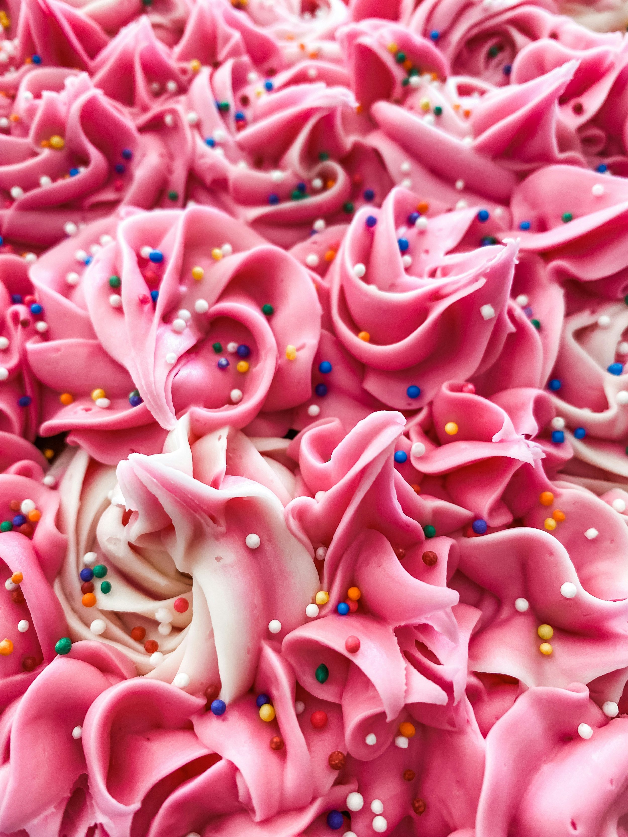 Close-up of pink frosting piped in rosette shapes decorated with multi-colored round sprinkles.