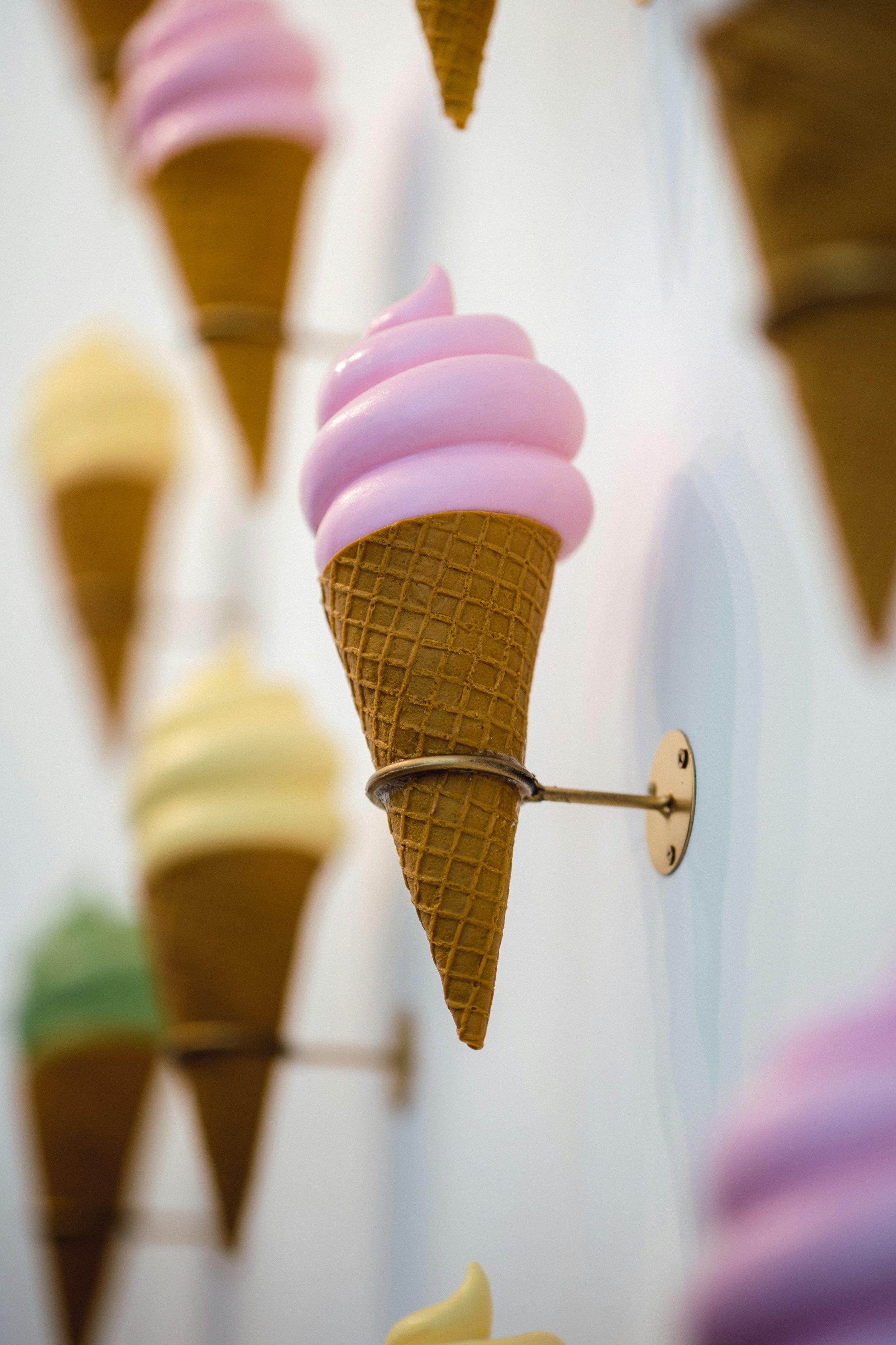 Close-up of pastel pink, yellow, purple, and green ice cream cone-shaped decorations mounted on a wall with metal brackets.