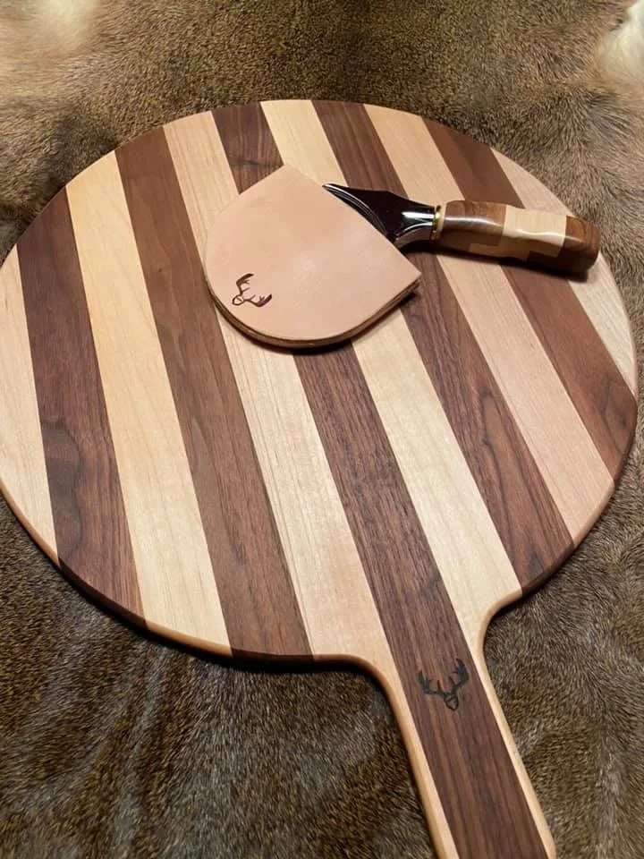 A striped wooden table tennis paddle with a small wooden block resting on it, and a knife with a wooden handle placed on top of the block, all on a furry surface.