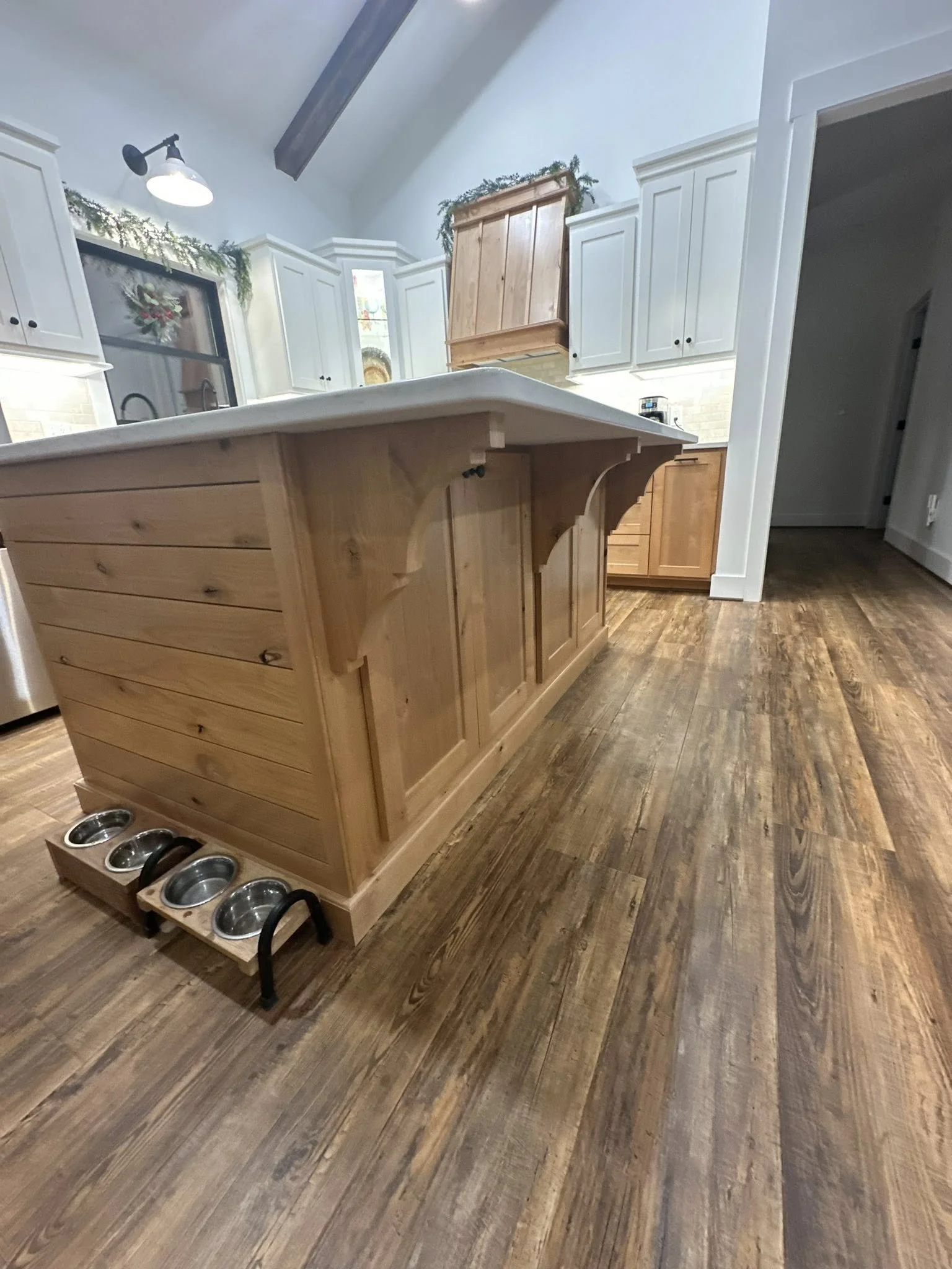 Wooden kitchen island with a white countertop and three pet food bowls underneath, in a kitchen with wooden floors and white cabinets.