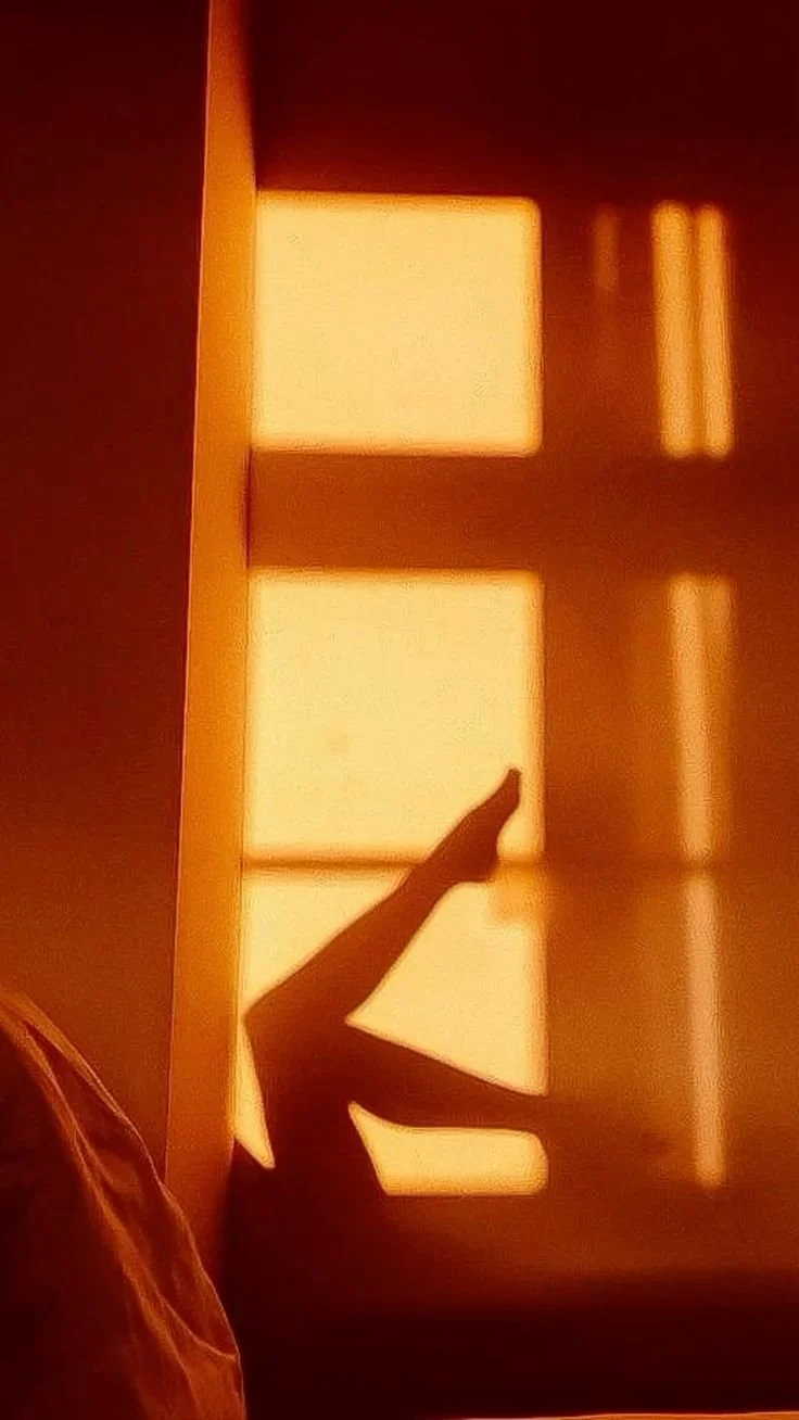 Shadow of a person’s leg and foot pointing upward on a wall with sunlight coming through window panes.