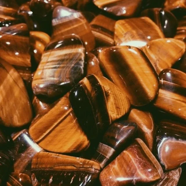 Close-up of polished brown and black tiger's eye stones with streaks of gold and dark brown.