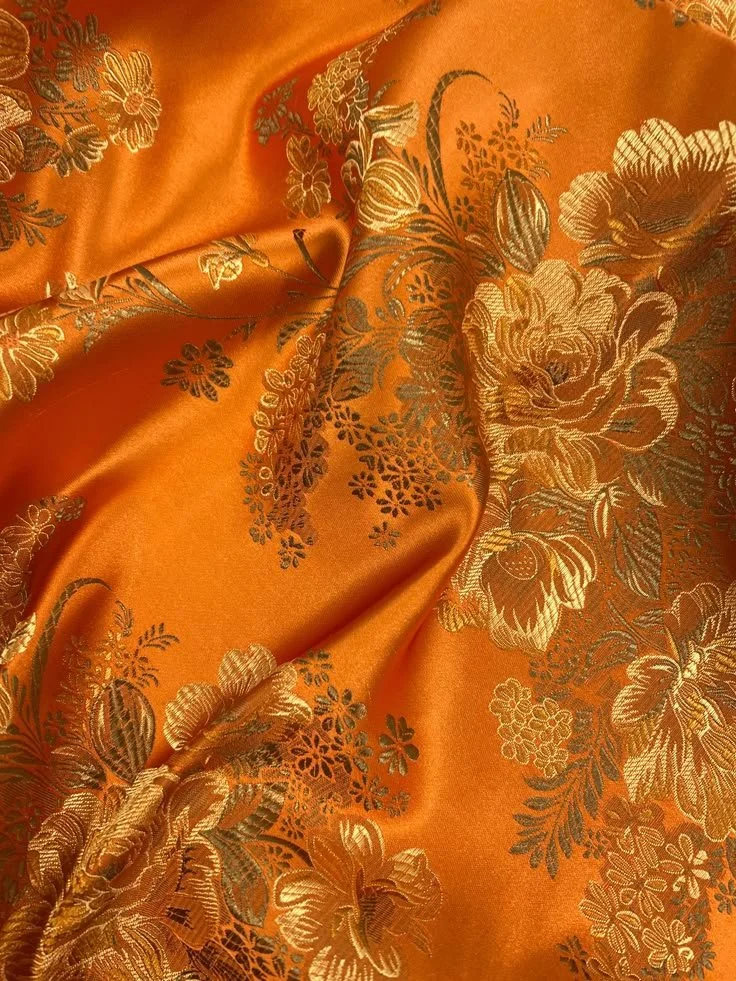 Close-up of orange satin fabric with intricate gold floral pattern.
