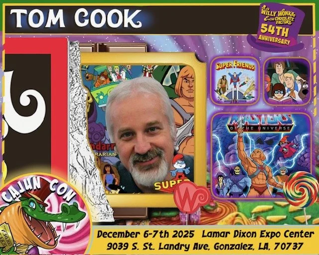 A person with a beard and short gray hair taking a selfie in front of a cartoon-themed display, featuring characters from 'He-Man,' 'Super Friends,' and 'Masters of the Universe,' with promotional information about a comic convention from December 6-
