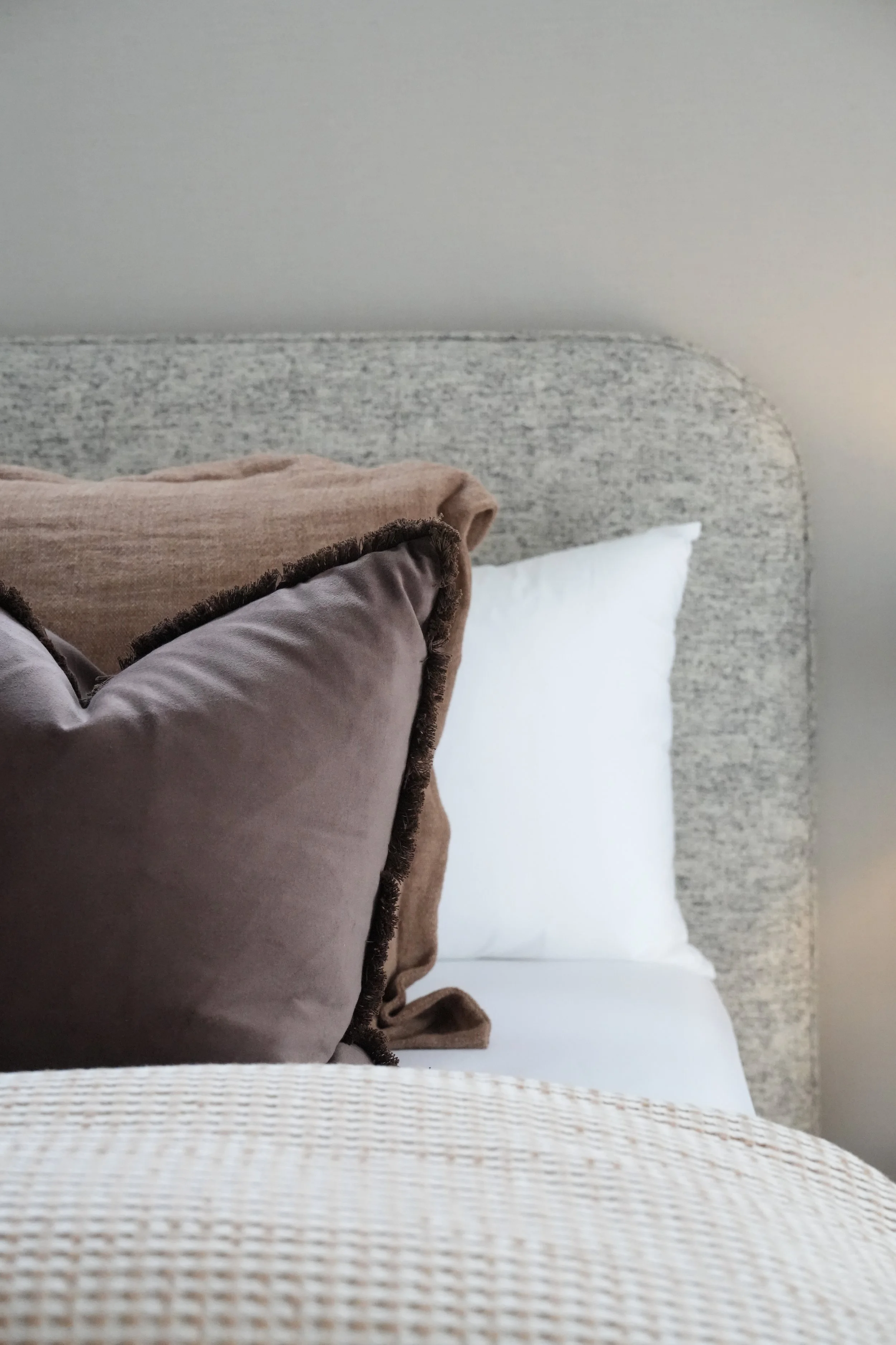 A neatly made bed with a textured gray headboard, white pillow, and folded brown and dusty pink blankets.