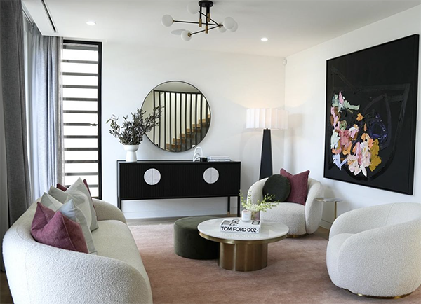 Living room with white and purple sofas, a round coffee table, and a black sideboard with a mirror above. Modern lamp and abstract art on the wall.