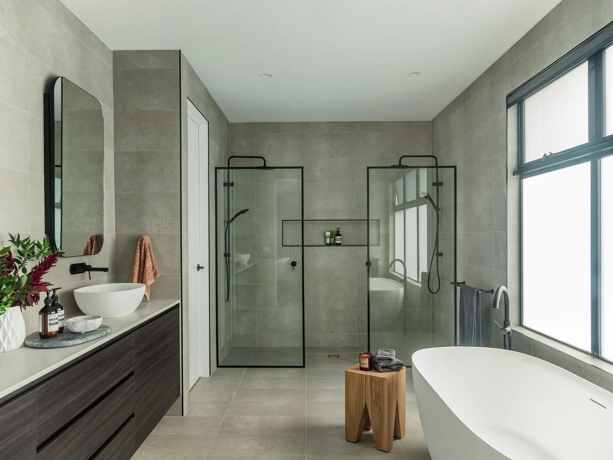 Modern bathroom with a floating vanity, vessel sink, large mirror, walk-in shower with glass doors, freestanding bathtub, and large windows.