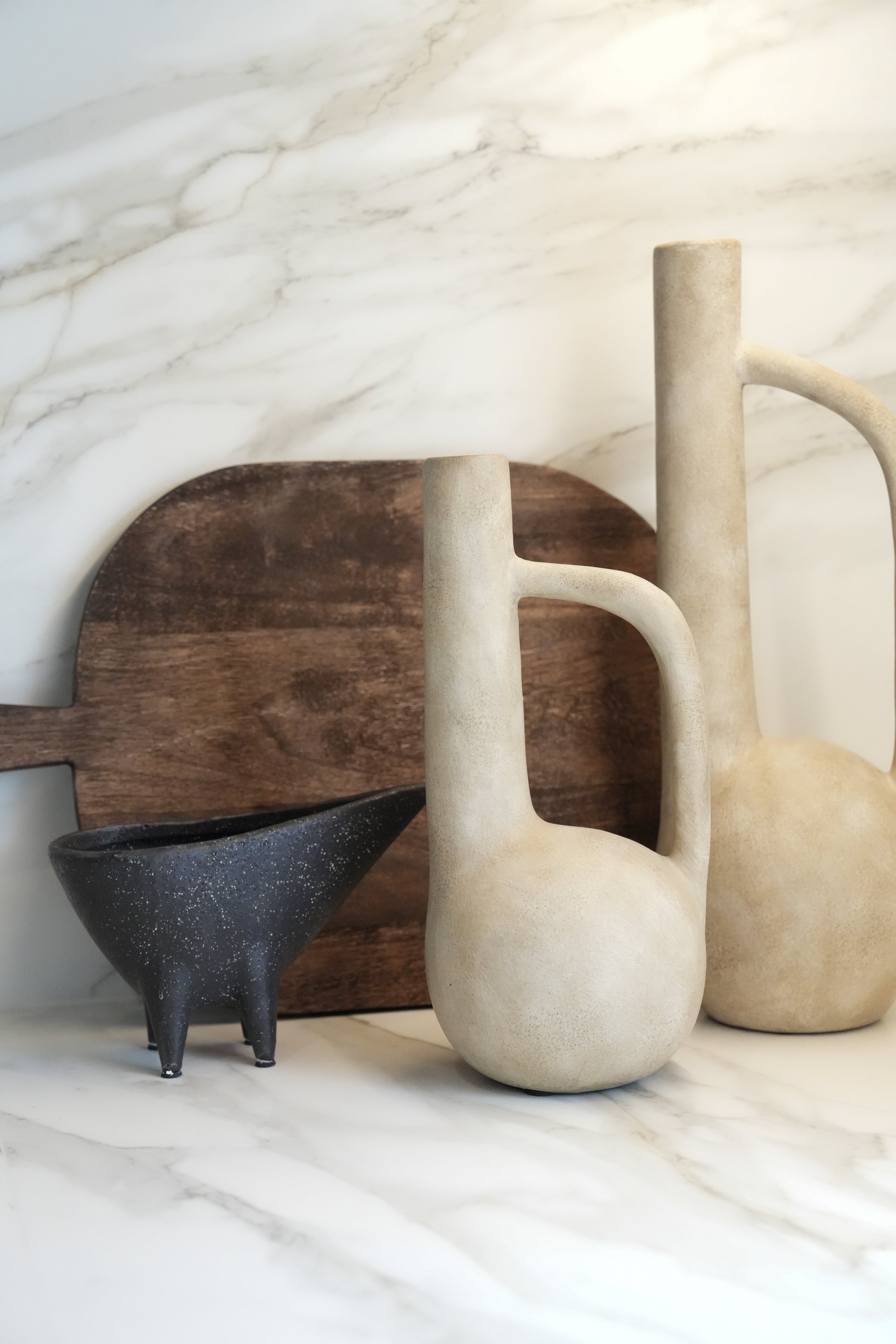 Decorative vases, a wooden cutting board, and a black speckled bowl arranged on a marble surface