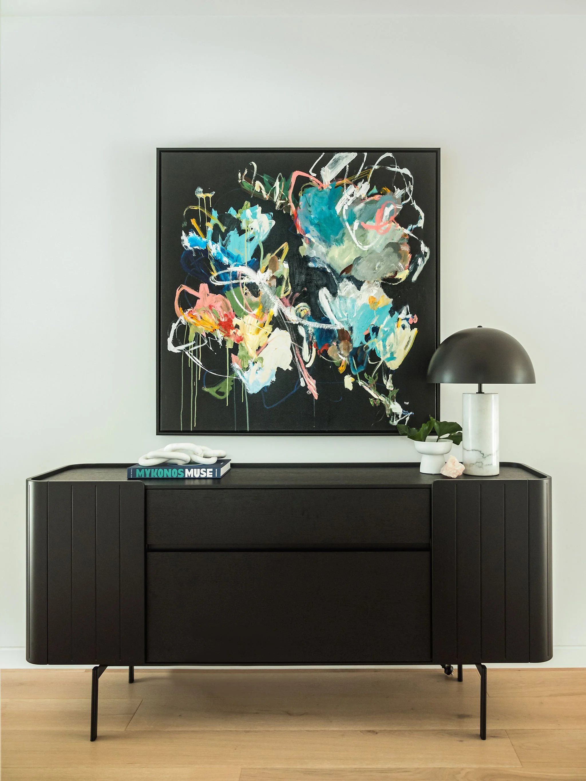 Black modern sideboard with decorative items and an abstract painting on the wall above, in a minimalist room.