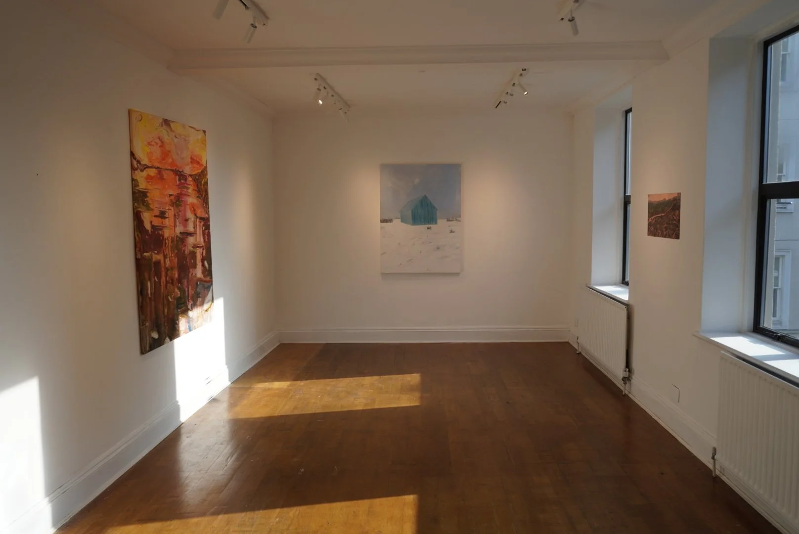 Gallery interior with wooden floors and white walls displaying three paintings, including a central snowy landscape with a turquoise structure.