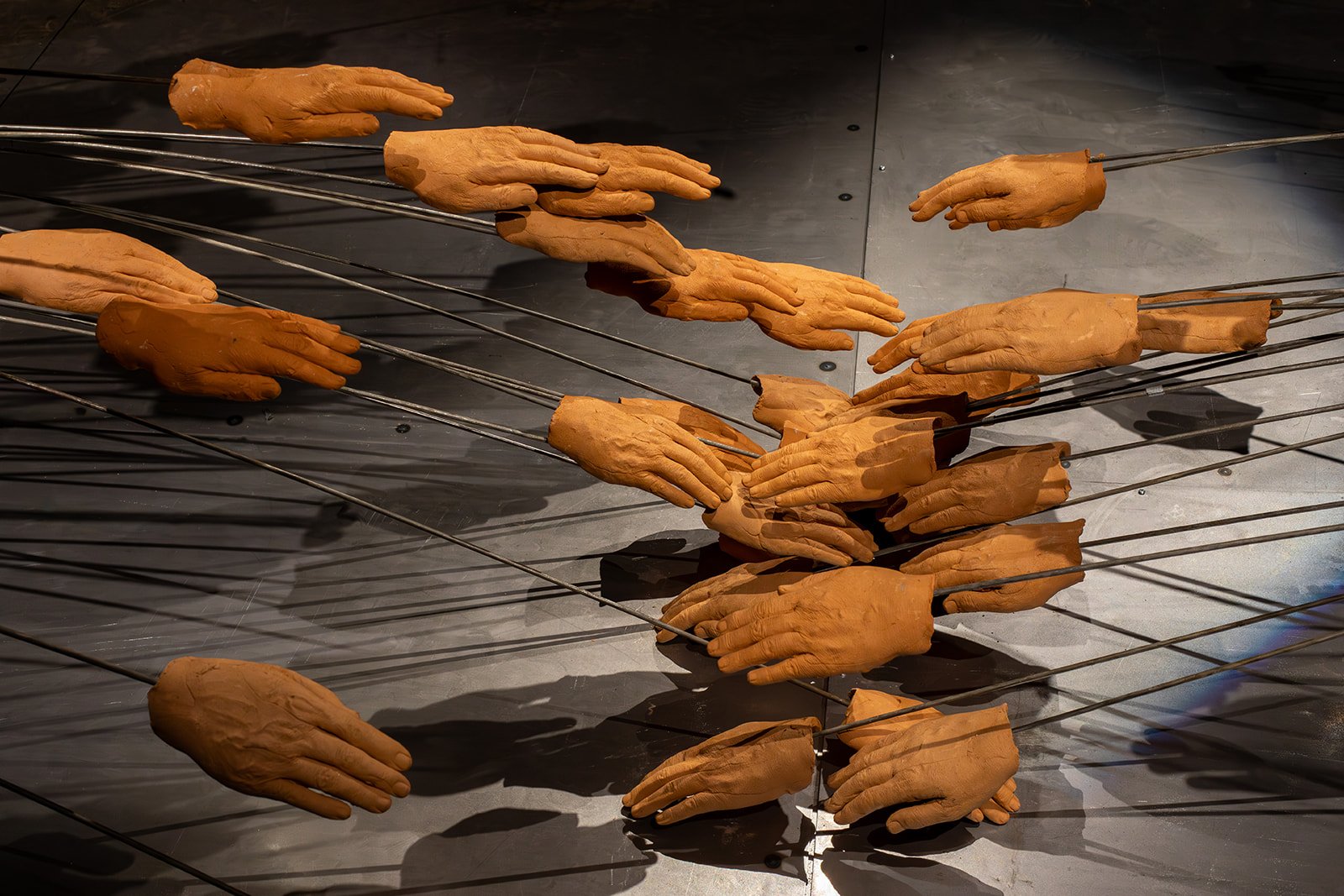 A sculpture consisting of clay hands affixed to flexible metal rods that bend down into each other meets at a convergence point, where the hands pile and lay on top of each other.