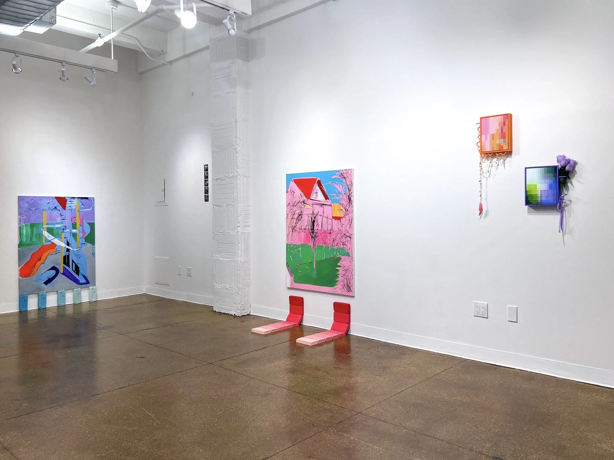 White-walled gallery with colorful paintings and small sculptural elements spaced across the walls, including a pink house painting and geometric works.