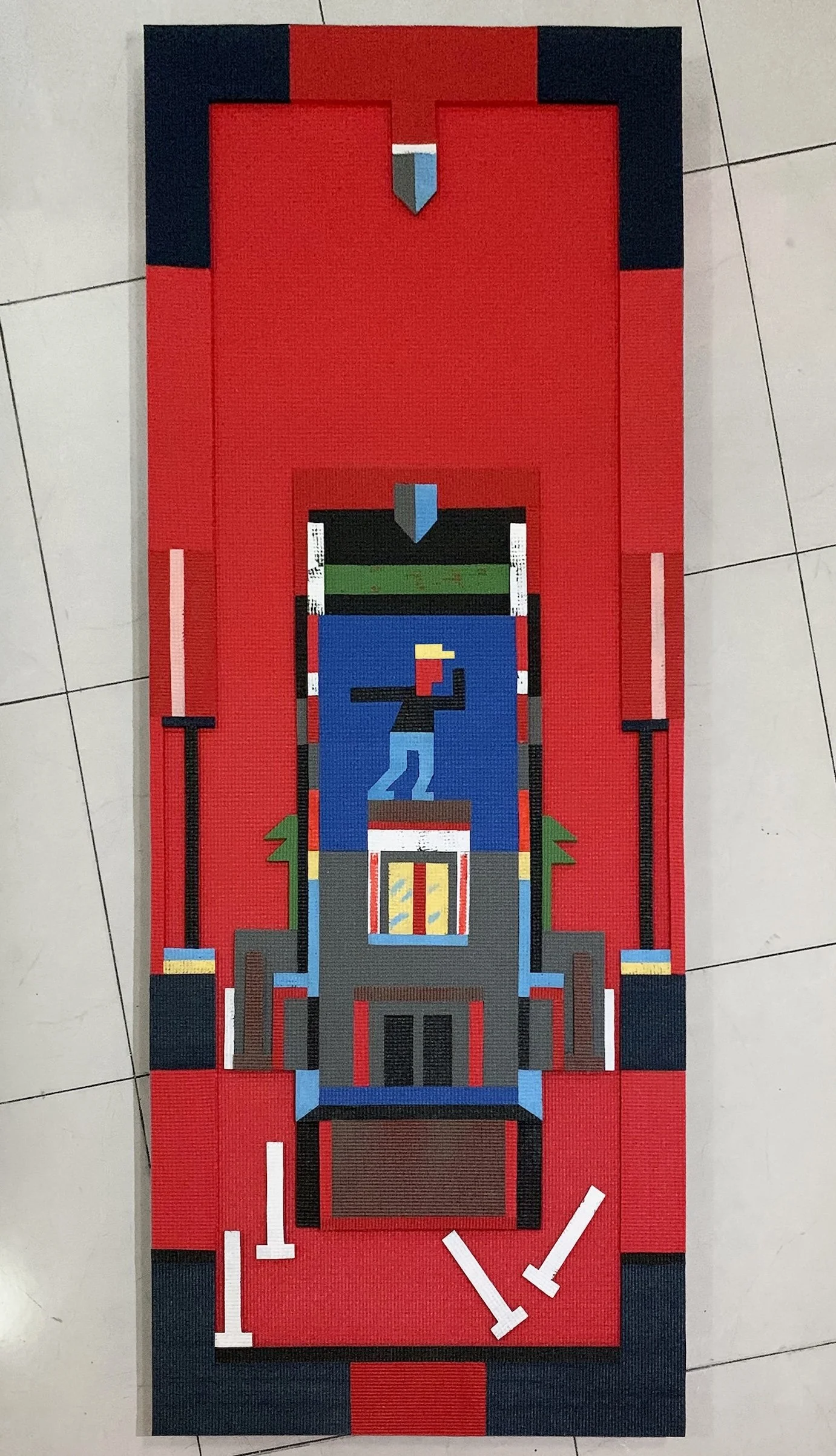 Rectangular textile work in red and black depicting a stylized architectural structure with a small pixelated figure standing atop a platform.