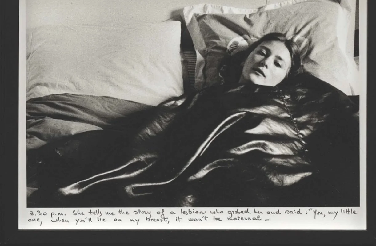 A black-and-white, black-framed photo of a person reclined in bed features text beneath that reads, "3.30 p.m. She tells me the story of a lesbian who grabed her and said: 'You, my little one, when you'll lie on my breast, it won't be maternal—'"