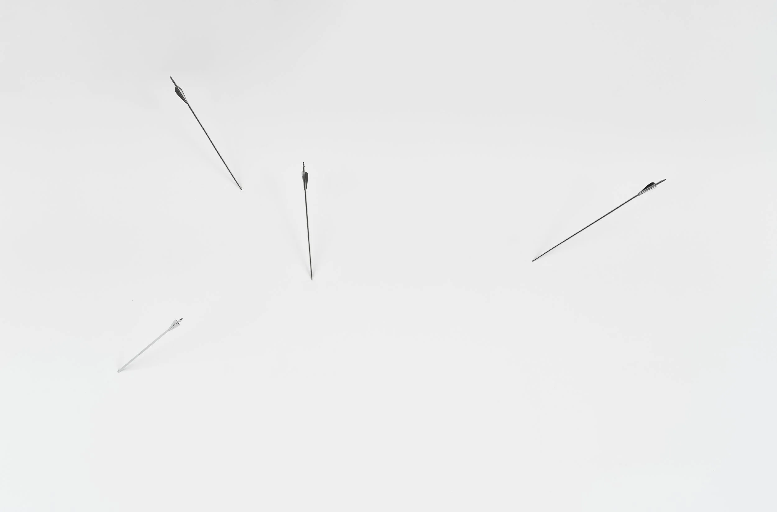 Four silver chrome arrows pierce and stick into a white wall at different angles.